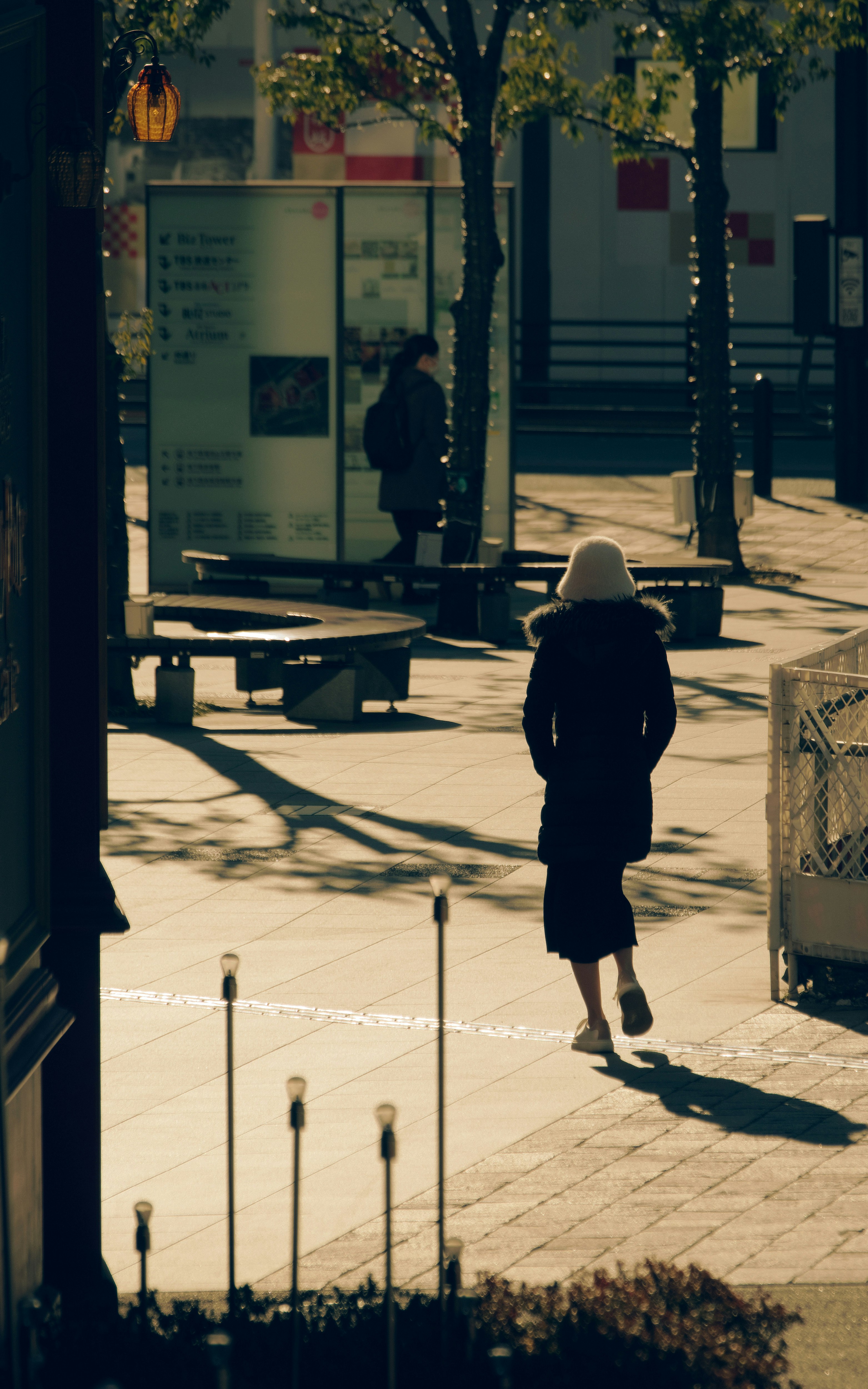 Frau, die auf der Straße mit Sonnenlicht-Schatten geht
