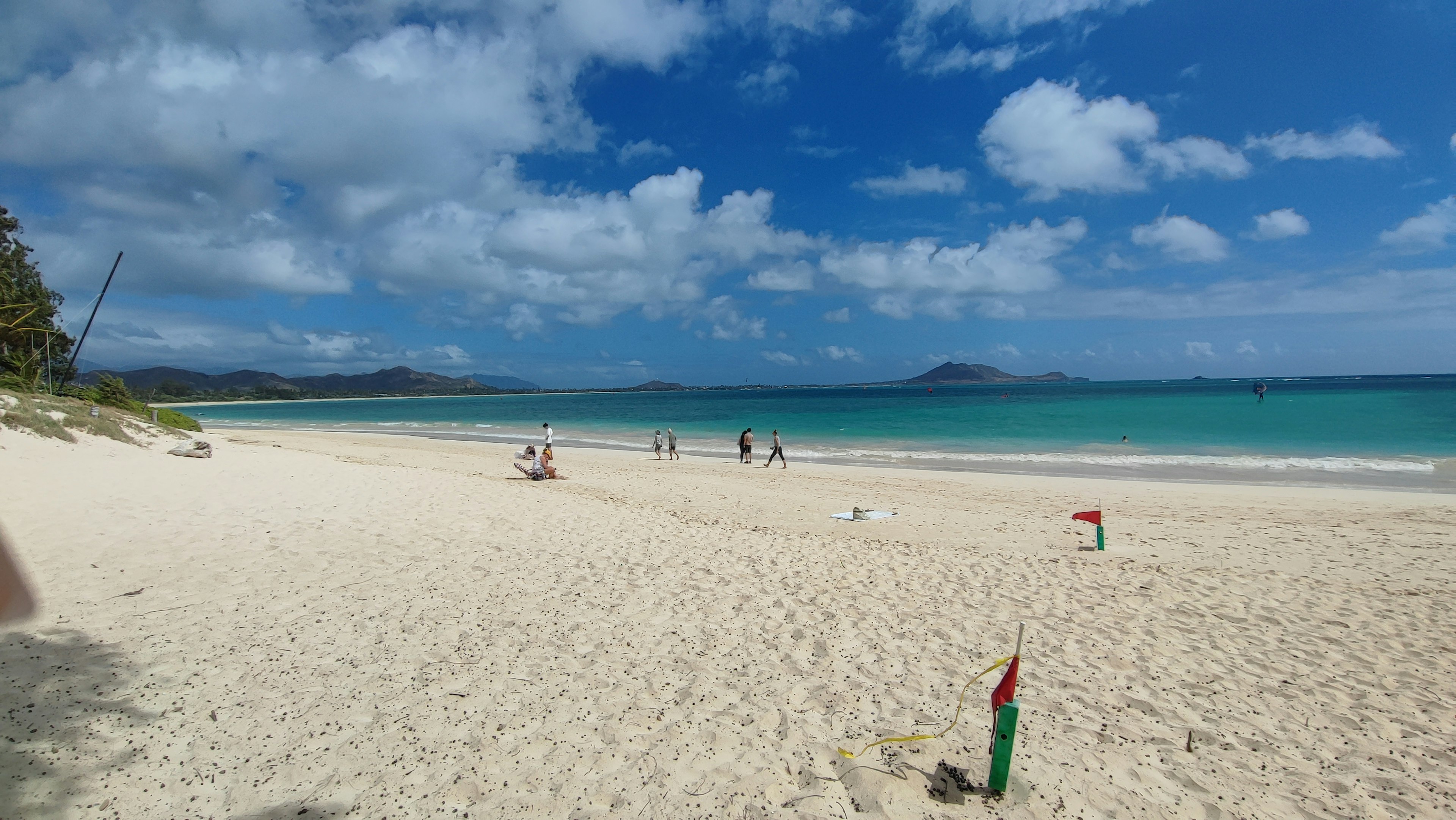 Escena de playa con cielo azul y arena blanca donde la gente se divierte