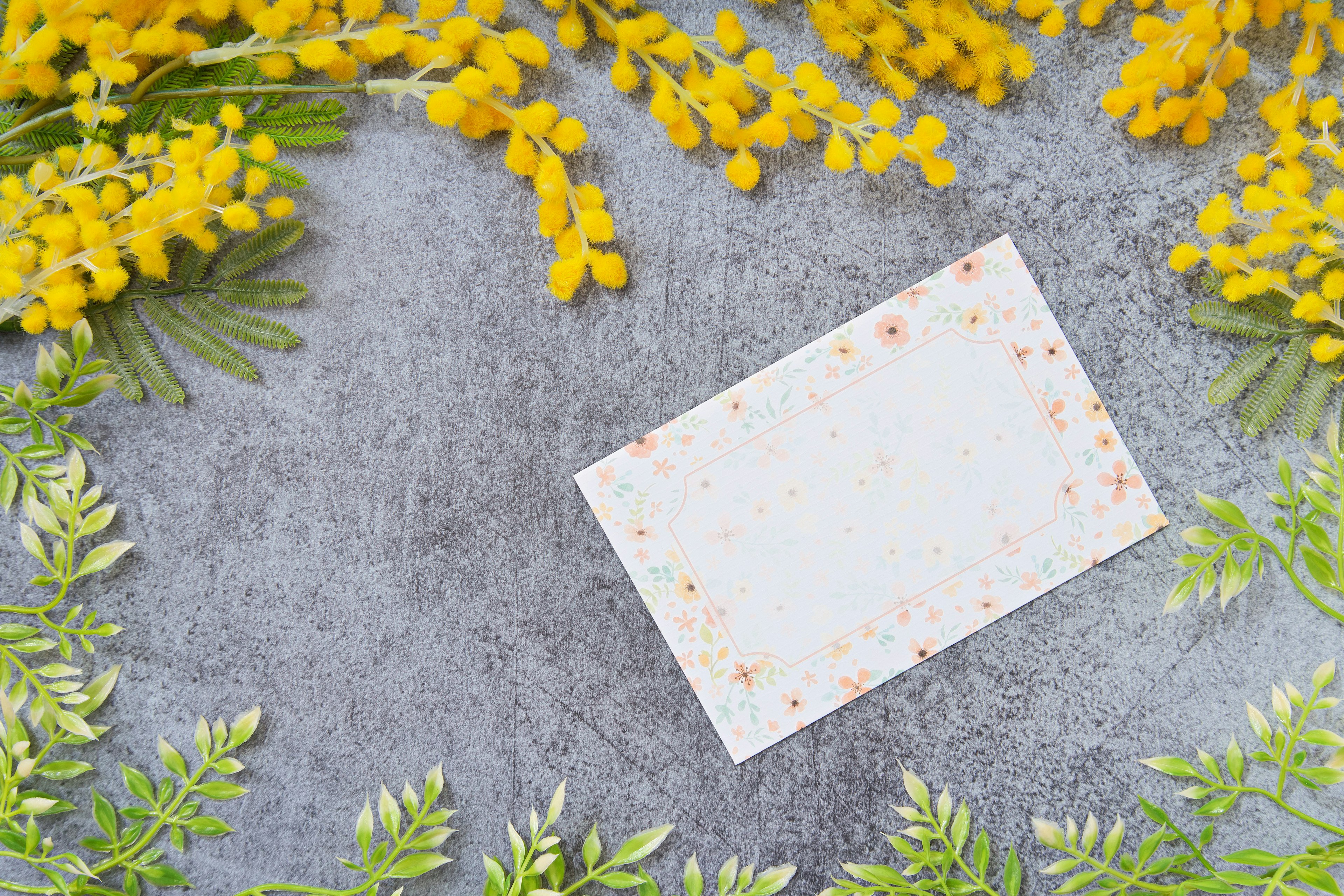 A white card surrounded by yellow mimosa flowers and green leaves