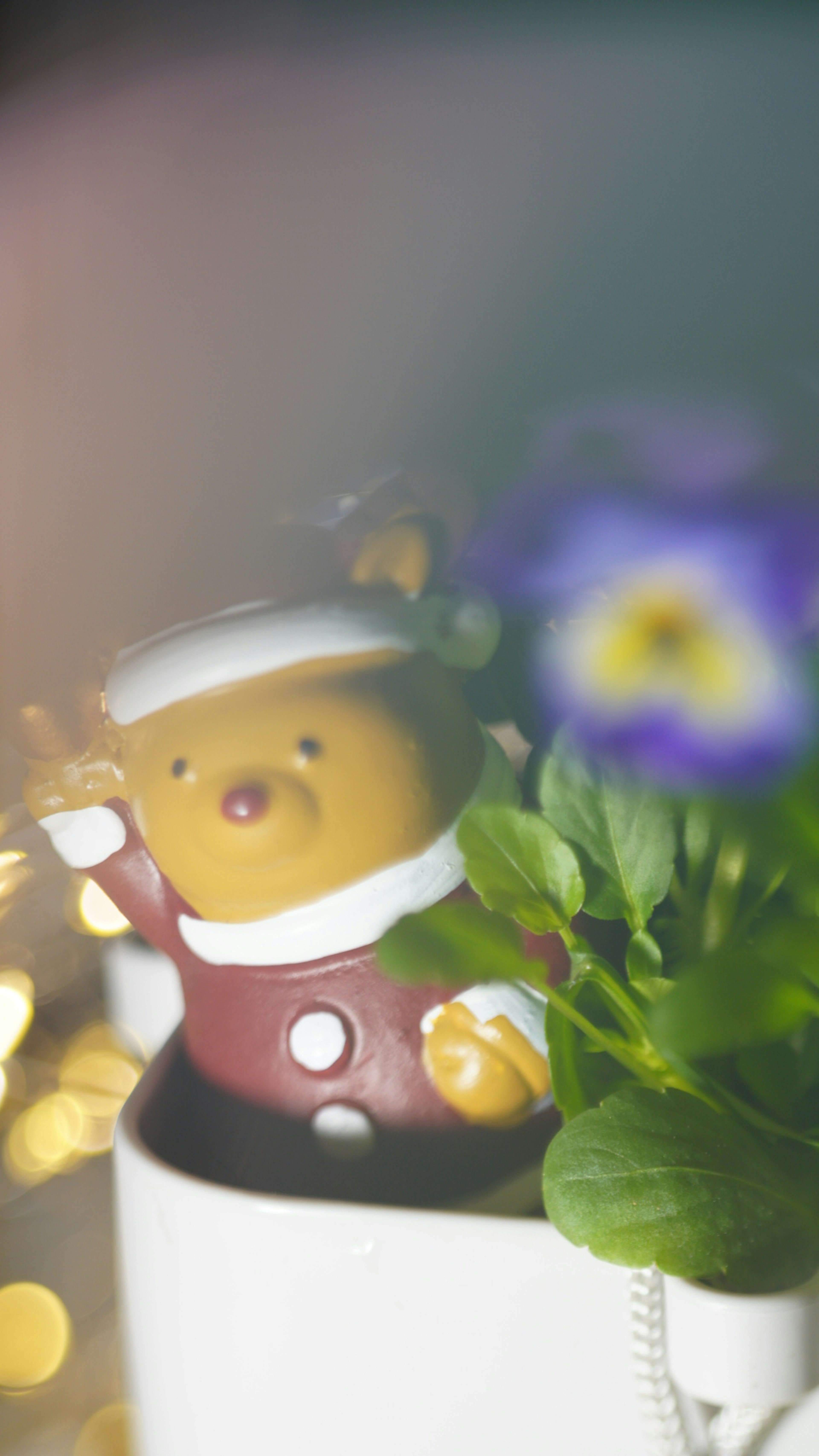 Brown bear figurine in a white cup with green leaves and purple flowers