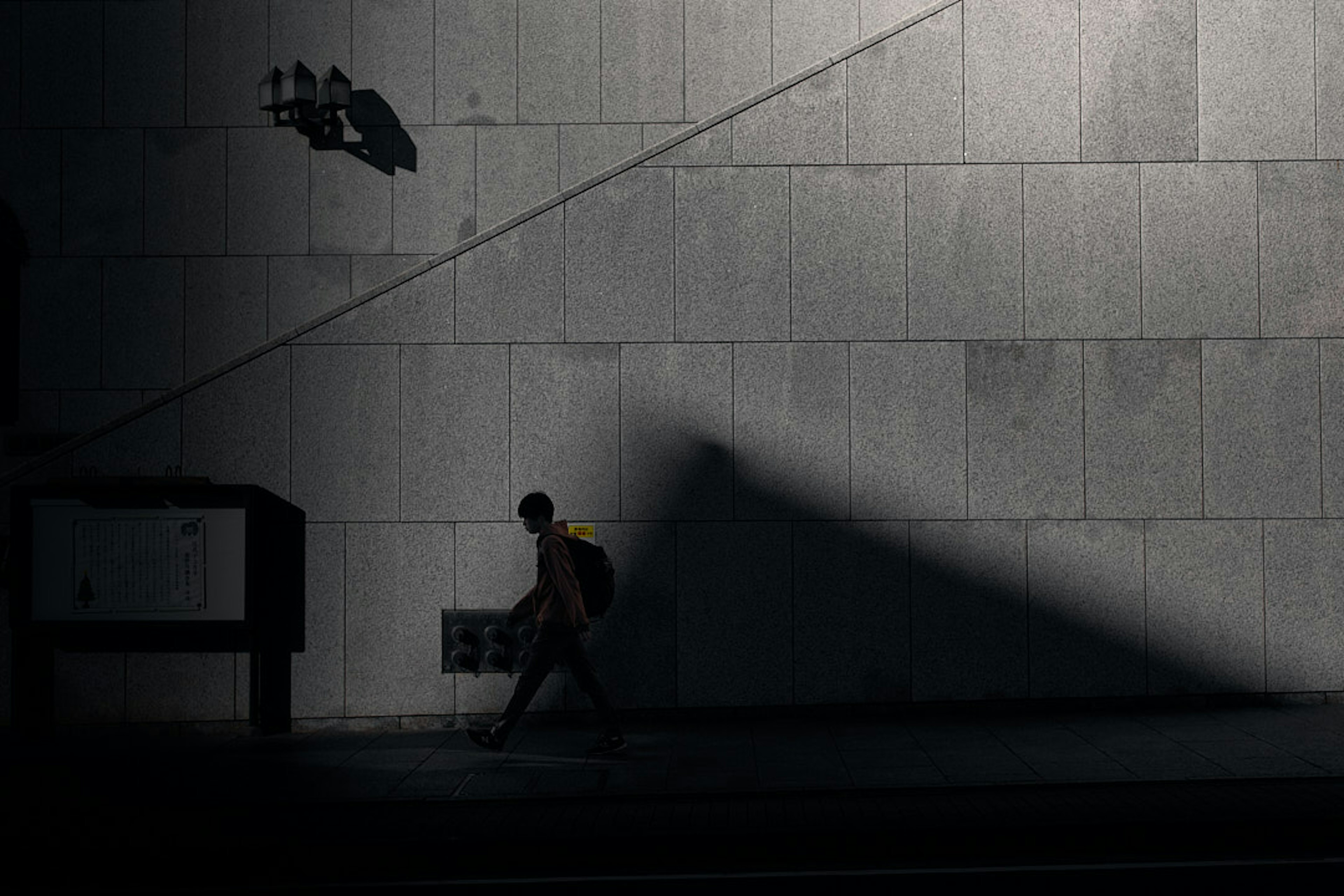 A person walking in front of a dark wall with striking shadow contrasts