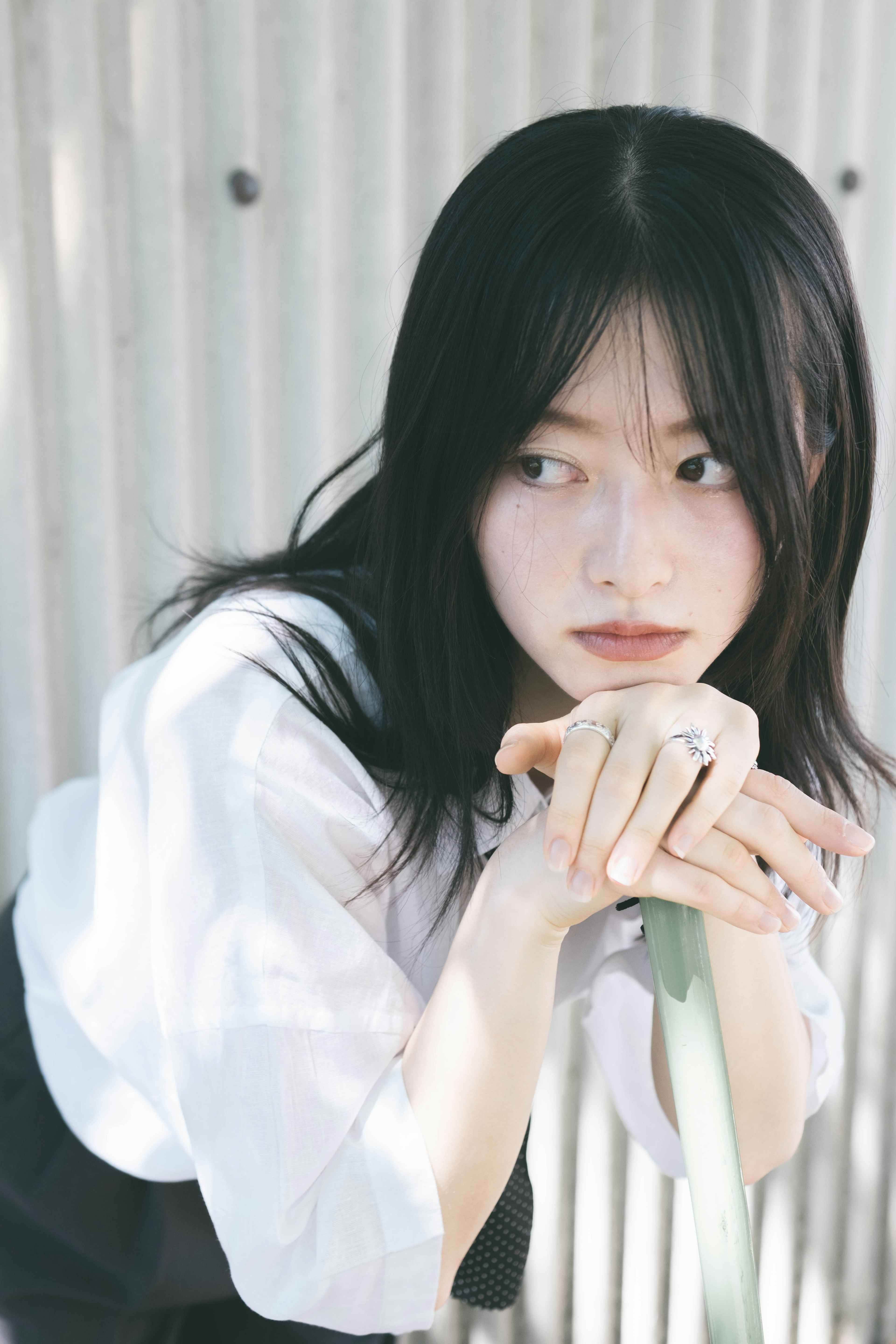 Young woman with long black hair resting her chin on her hands wearing a white shirt