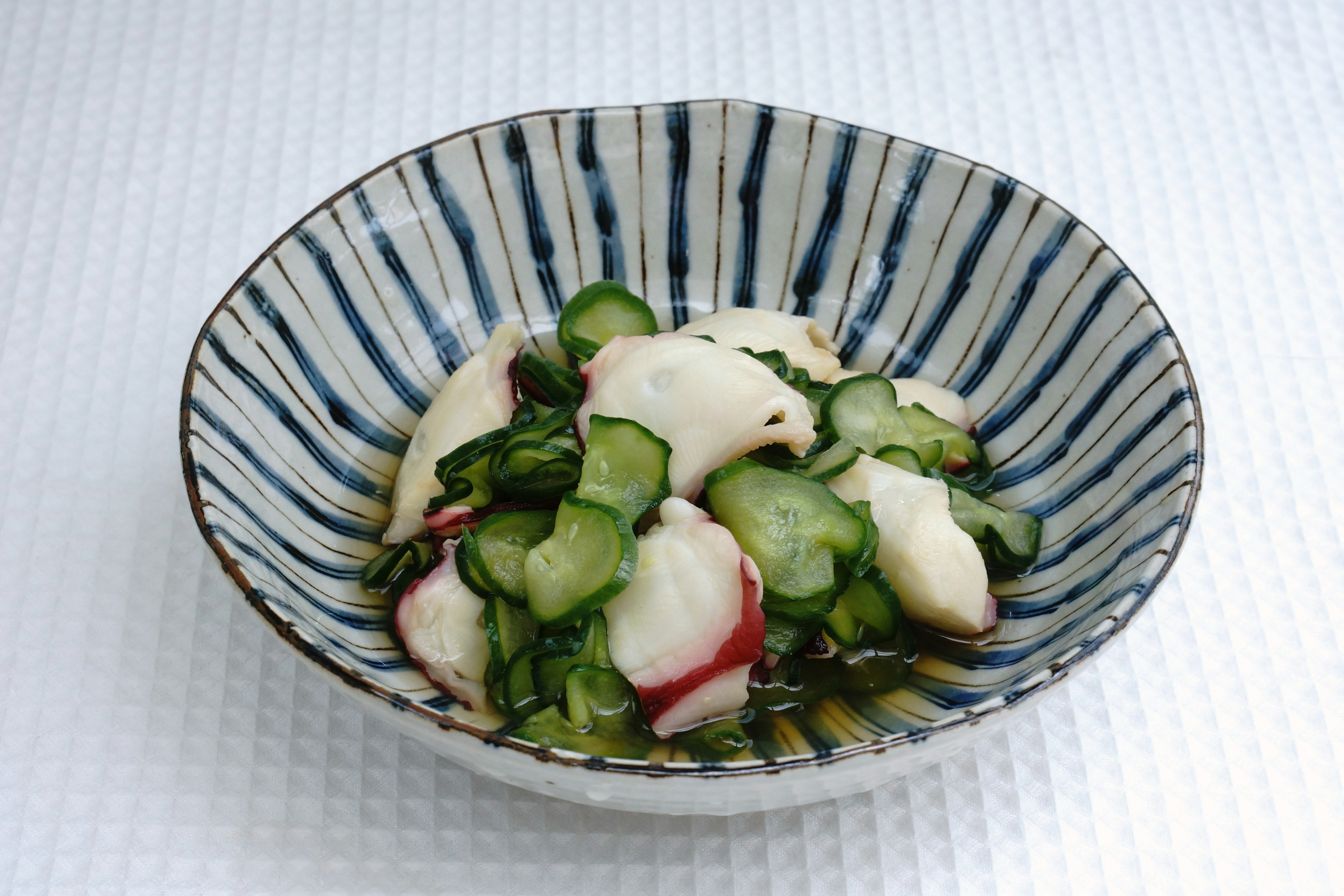 Ensalada de pepino y pescado blanco servida en un tazón a rayas