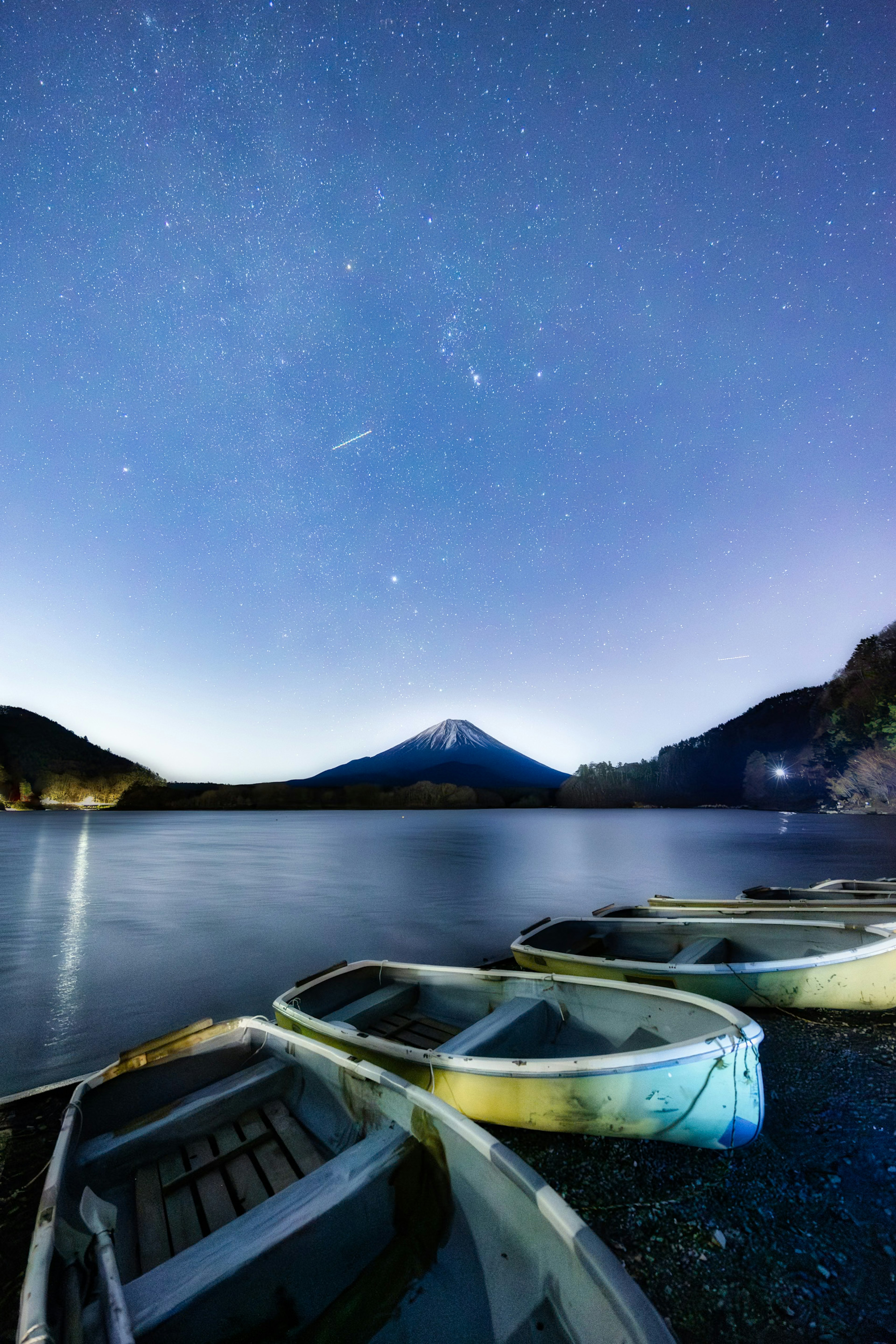 Vista serena de pequeños botes alineados en la orilla de un lago bajo un hermoso cielo estrellado