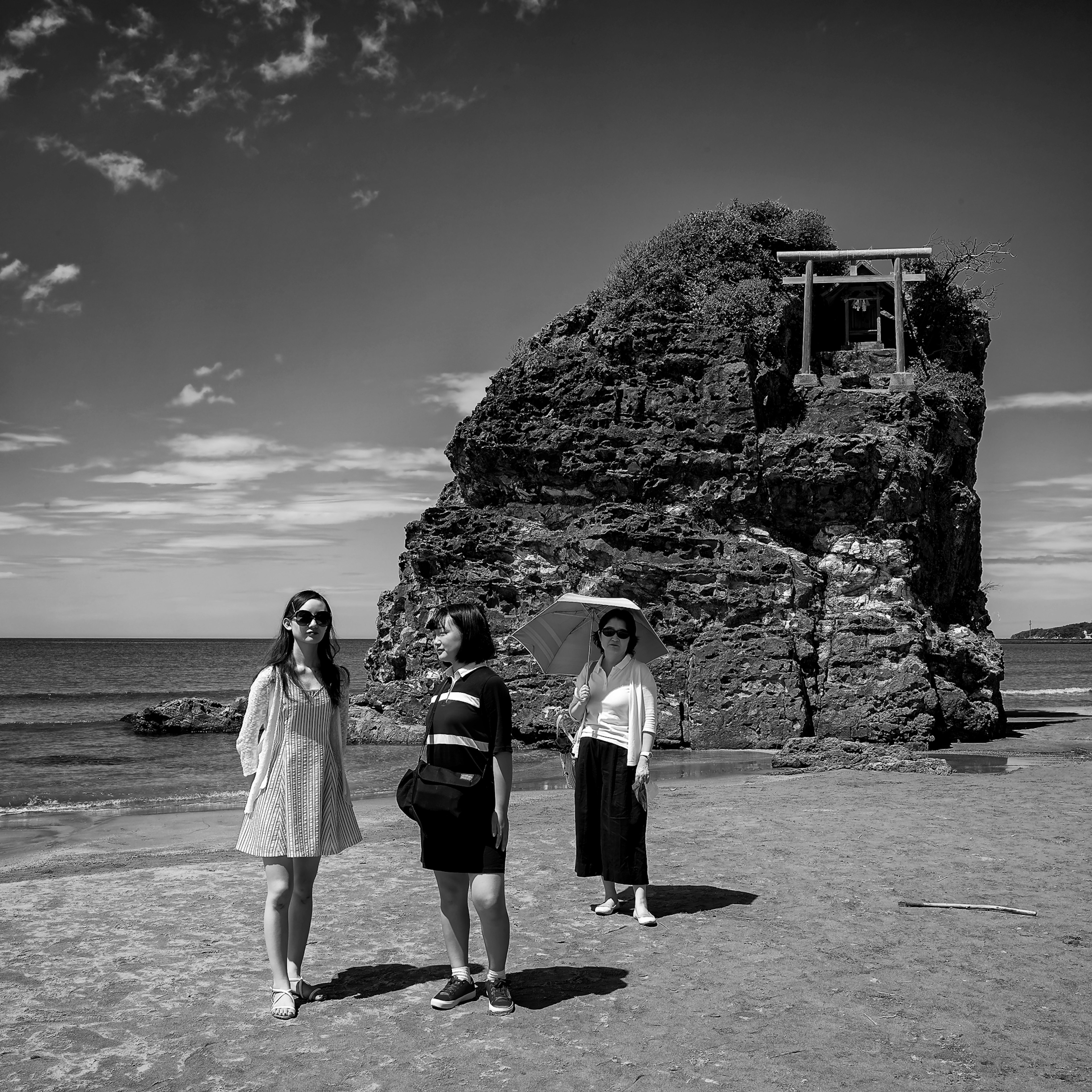 Women standing on the beach with a rock formation featuring a shrine