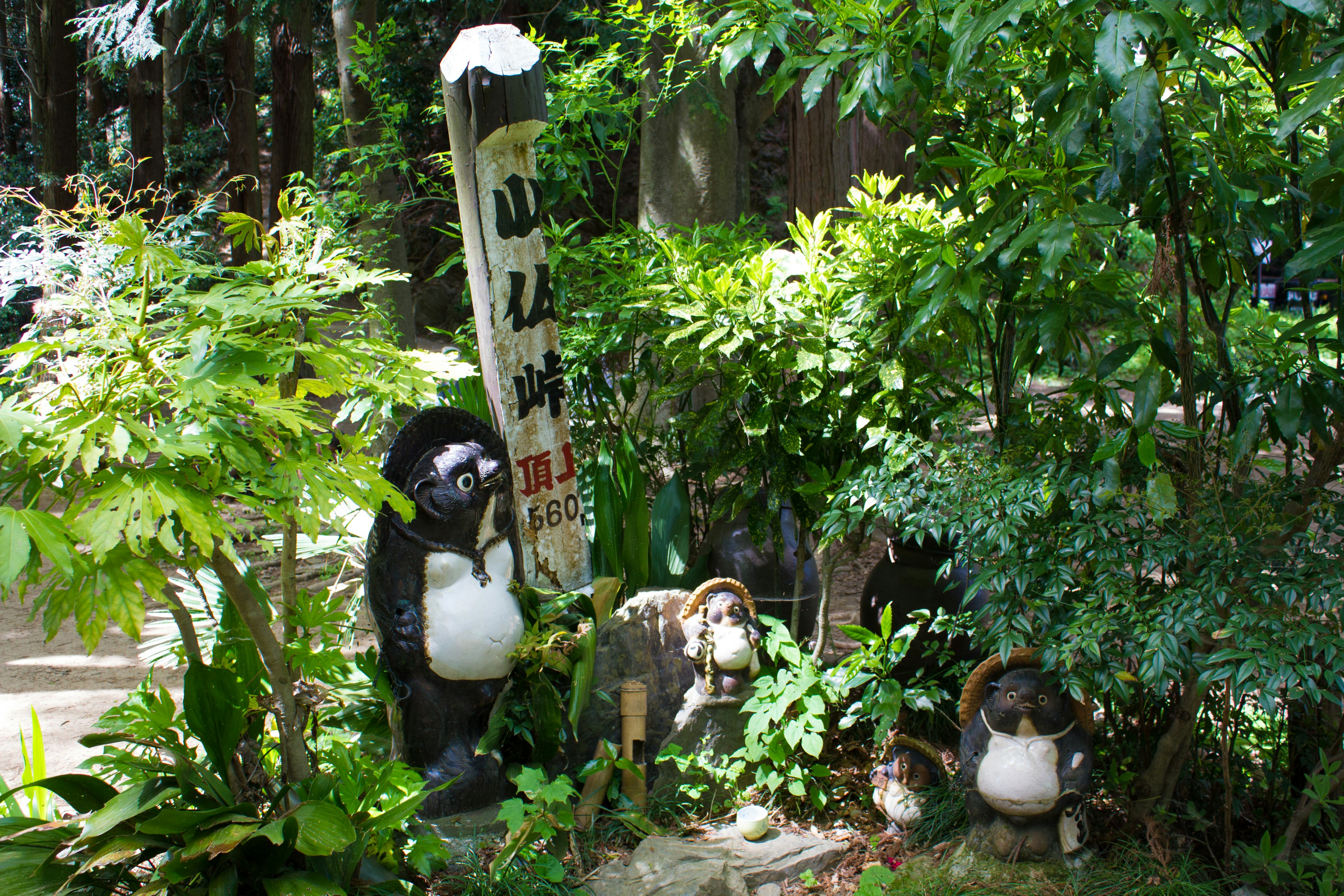 Tanuki-Skulpturen und ein Schild in einem üppigen Garten