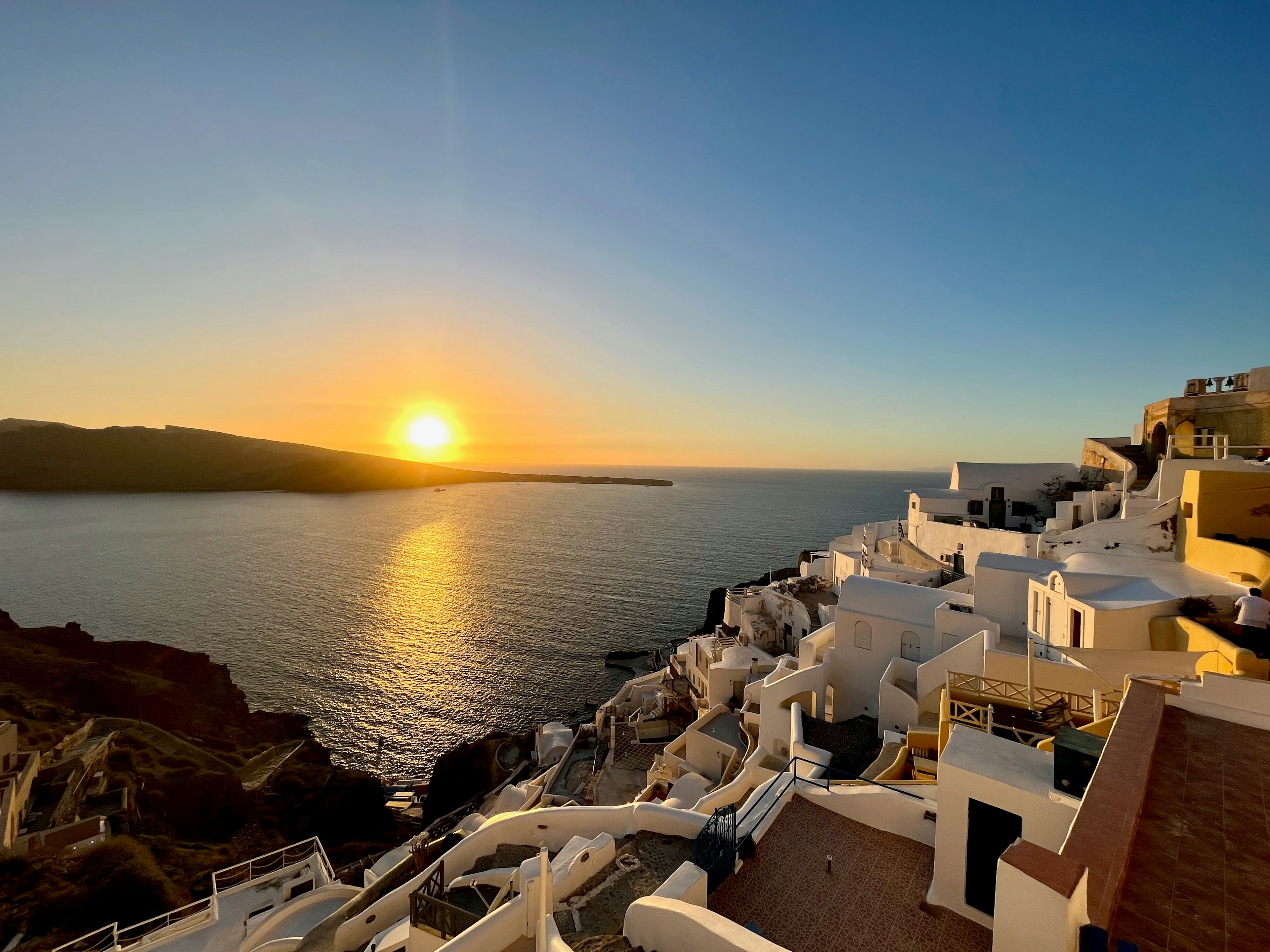 Weiße Gebäude entlang der Küste von Santorini mit einem Sonnenuntergang