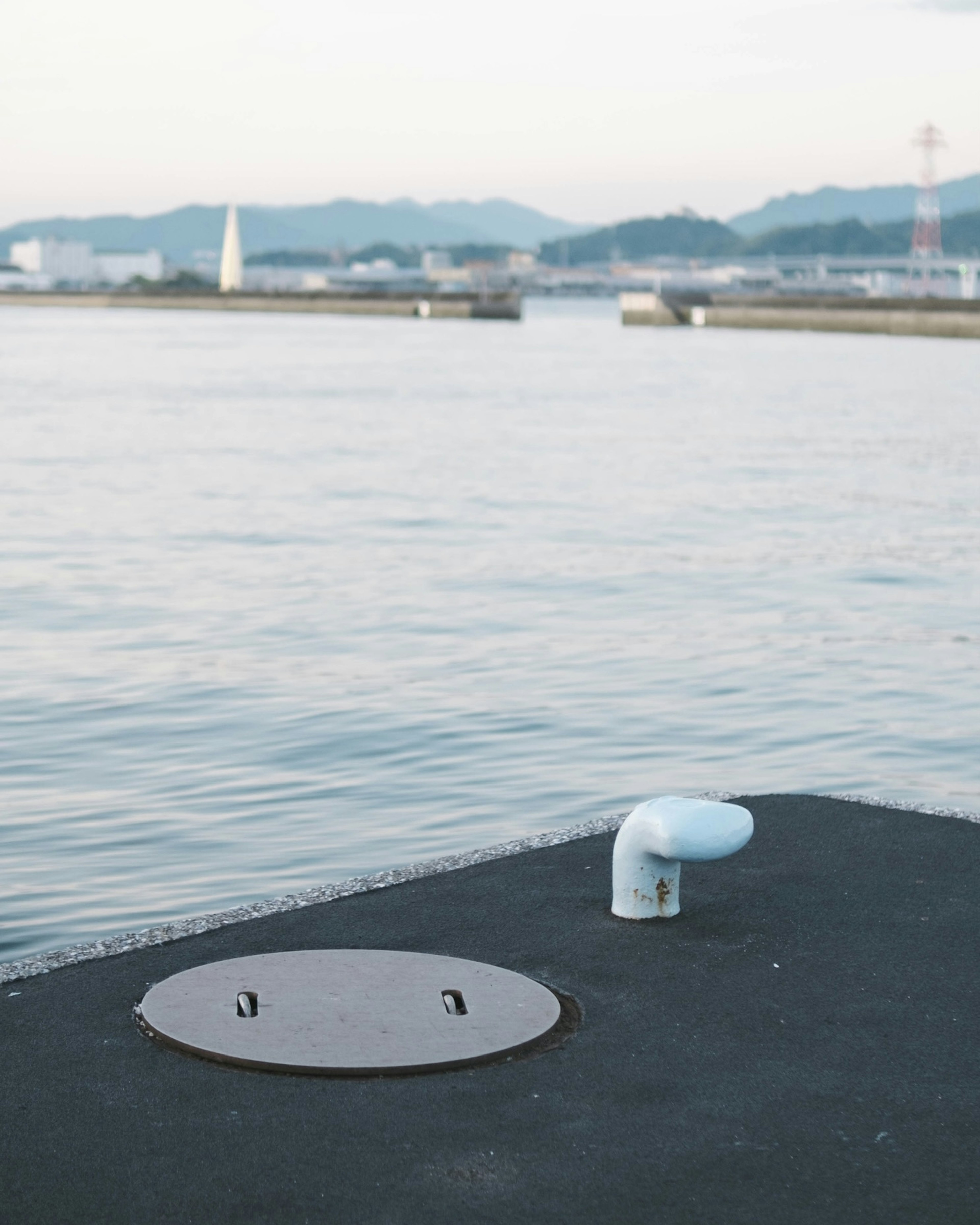 静かな水面の近くにある金属の蓋と白いパイプがある桟橋の風景