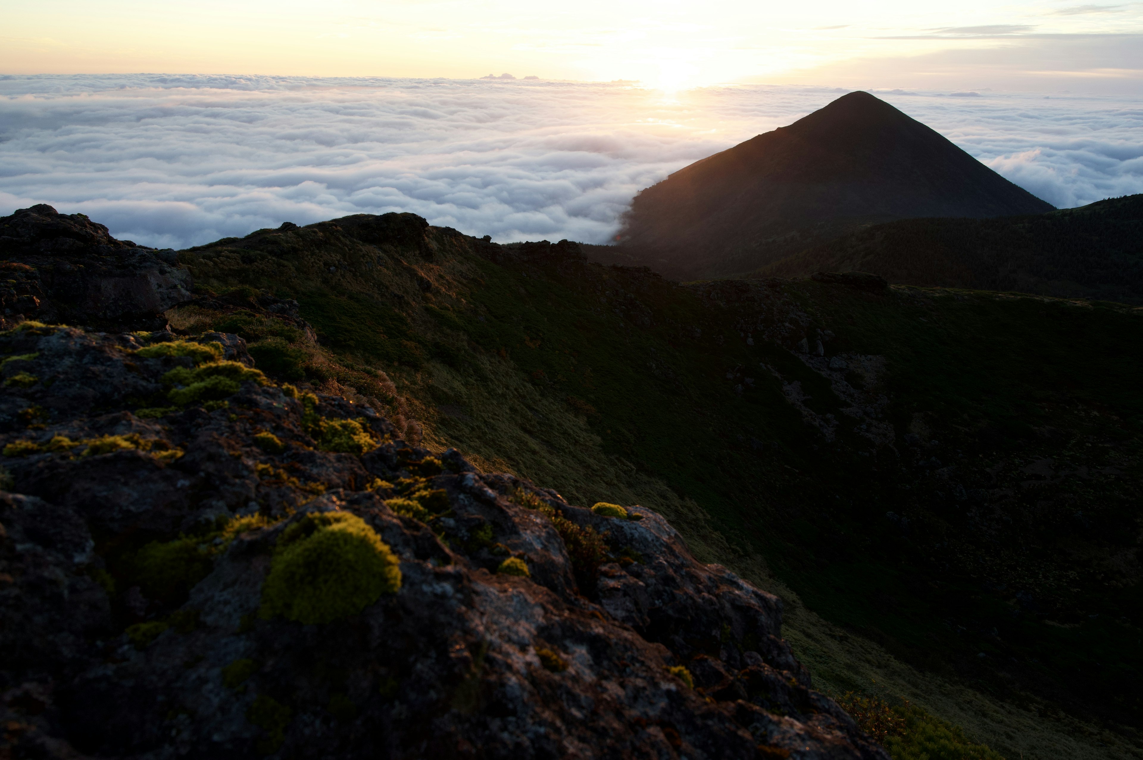 Mountain peak illuminated by sunlight above a sea of clouds with green moss