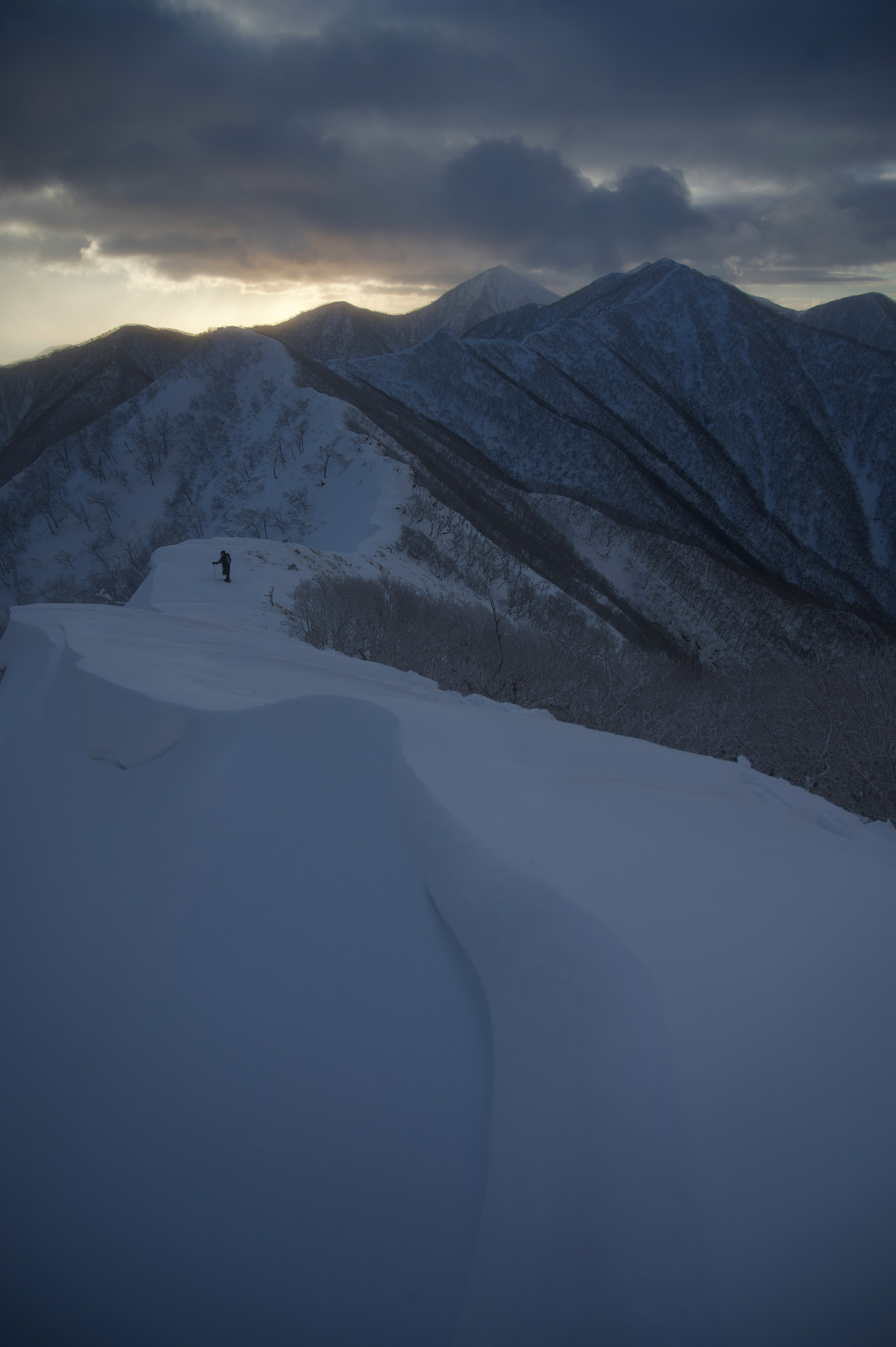 A hiker on a snow-covered mountain ridge under a cloudy sky