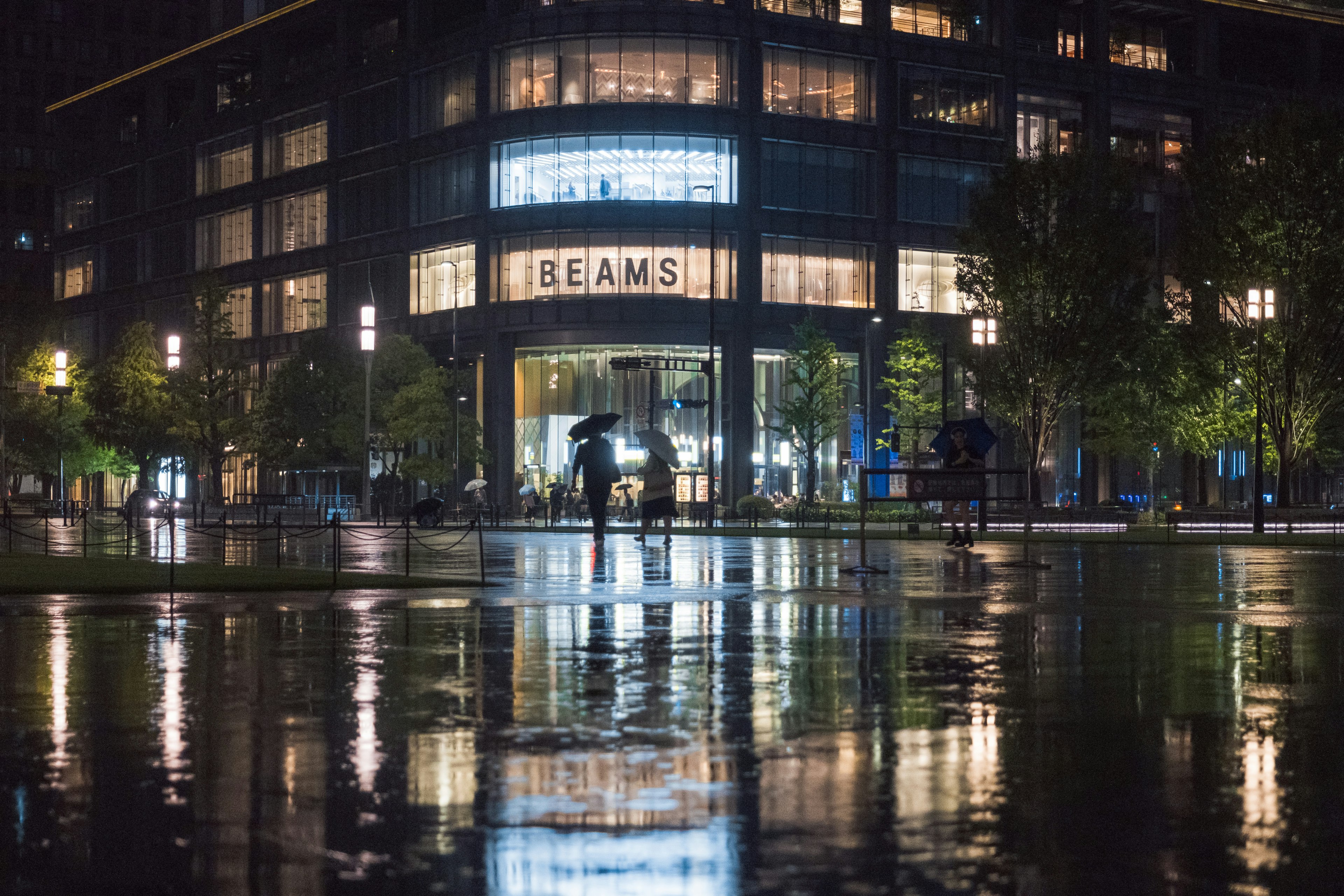 Edificio BEAMS iluminado por la noche con reflejos en los charcos