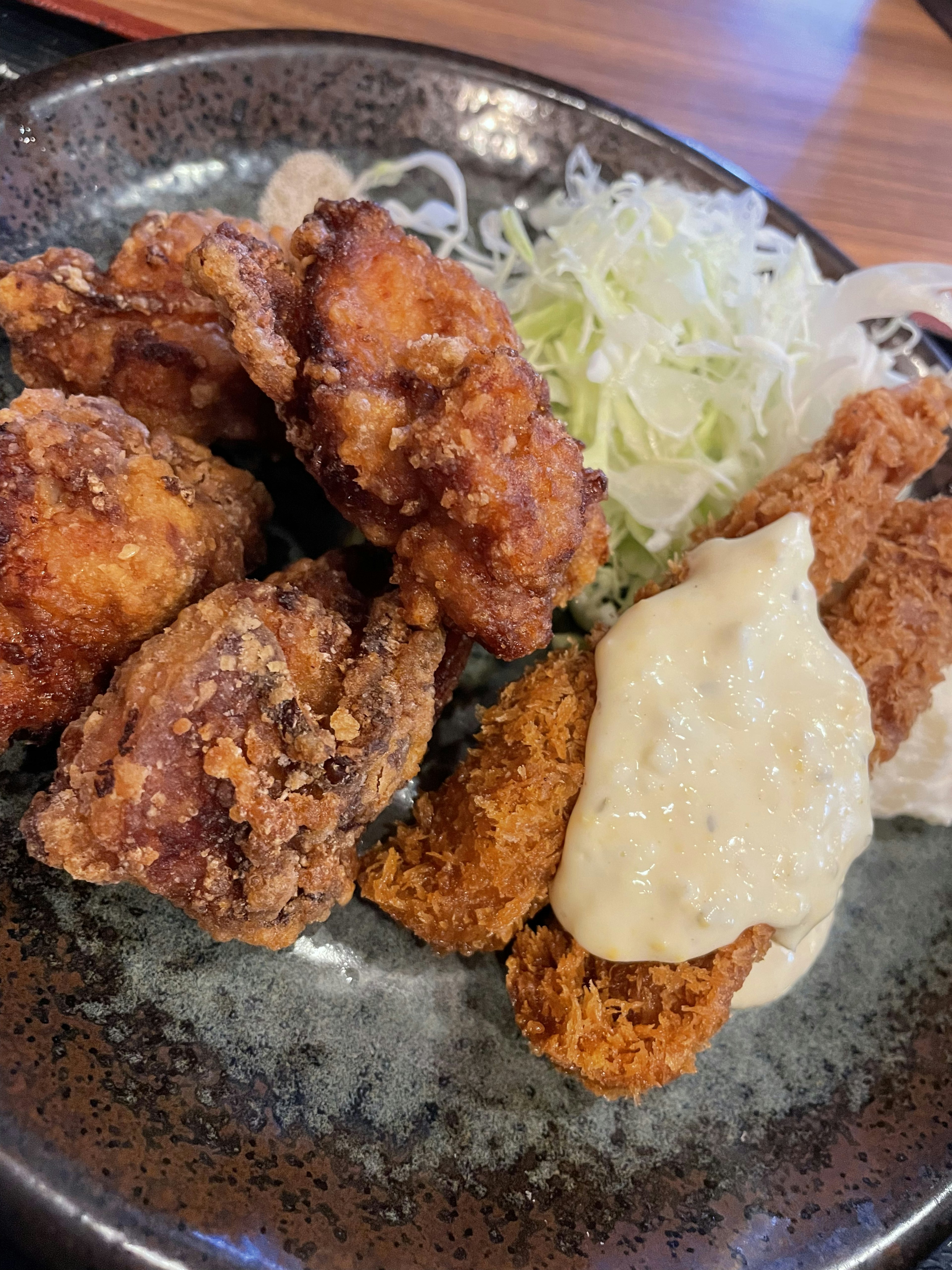 Fried chicken pieces served on a black plate with shredded cabbage