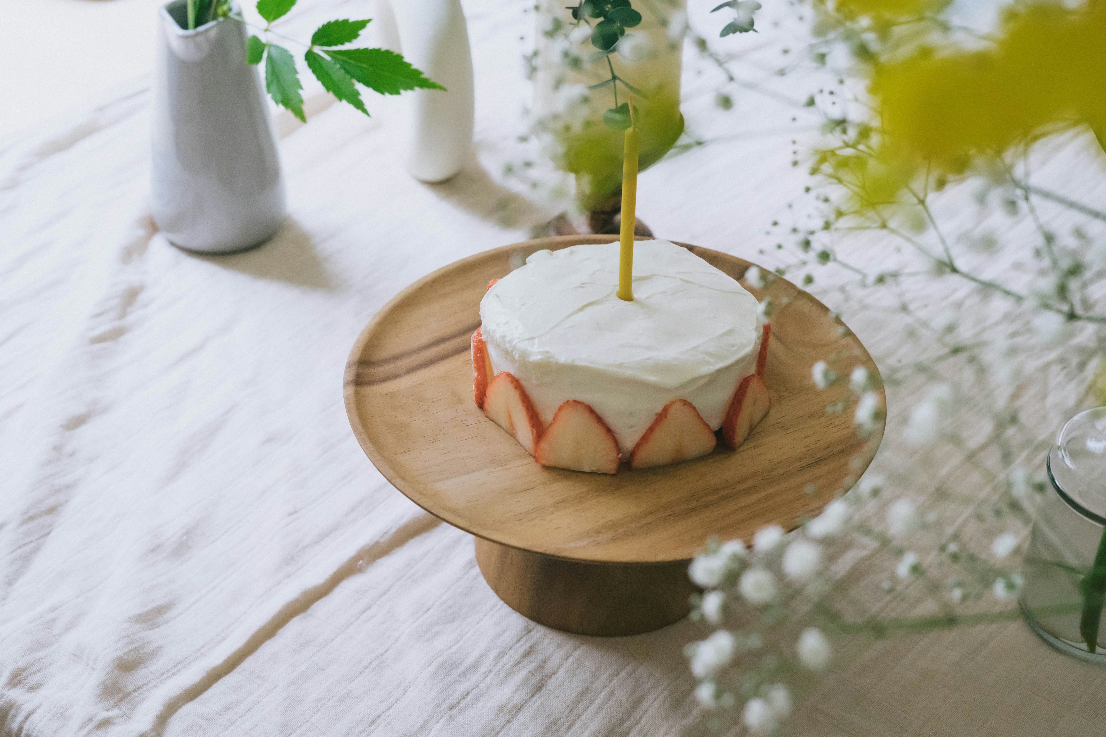 A cake with white cream and strawberry decoration on a wooden cake stand