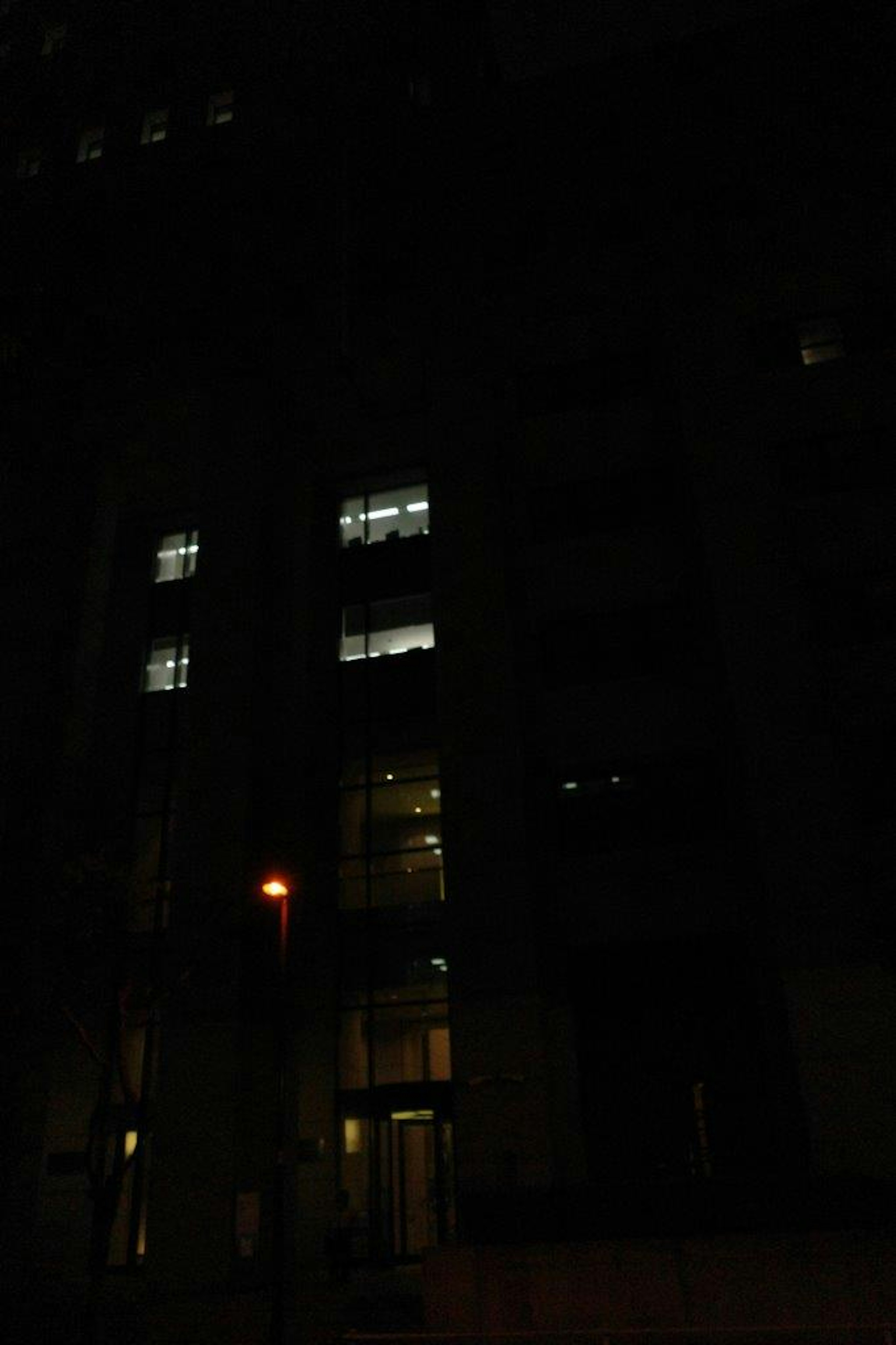 Dark building exterior with lights visible in several windows