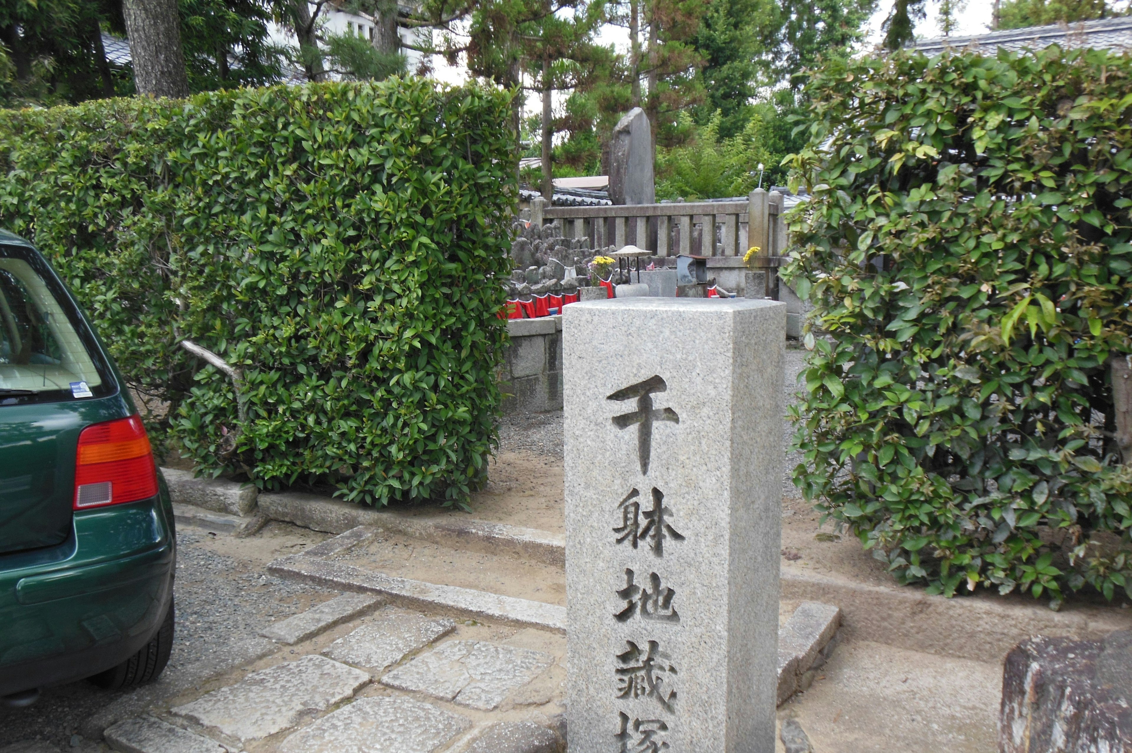 Stone monument surrounded by green hedges with a parked car