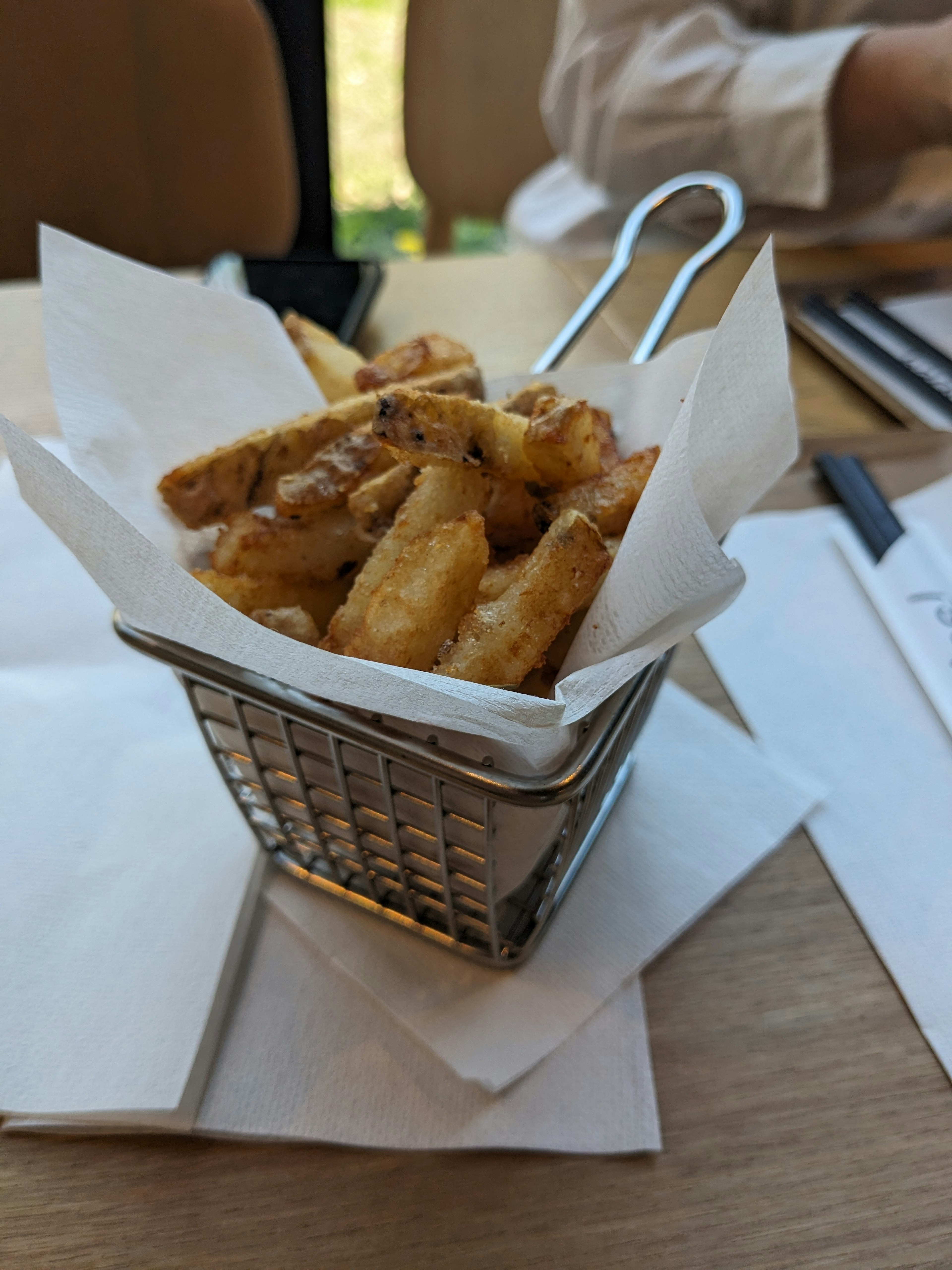 Piccolo cestino di metallo pieno di patate fritte dorate avvolte in carta bianca