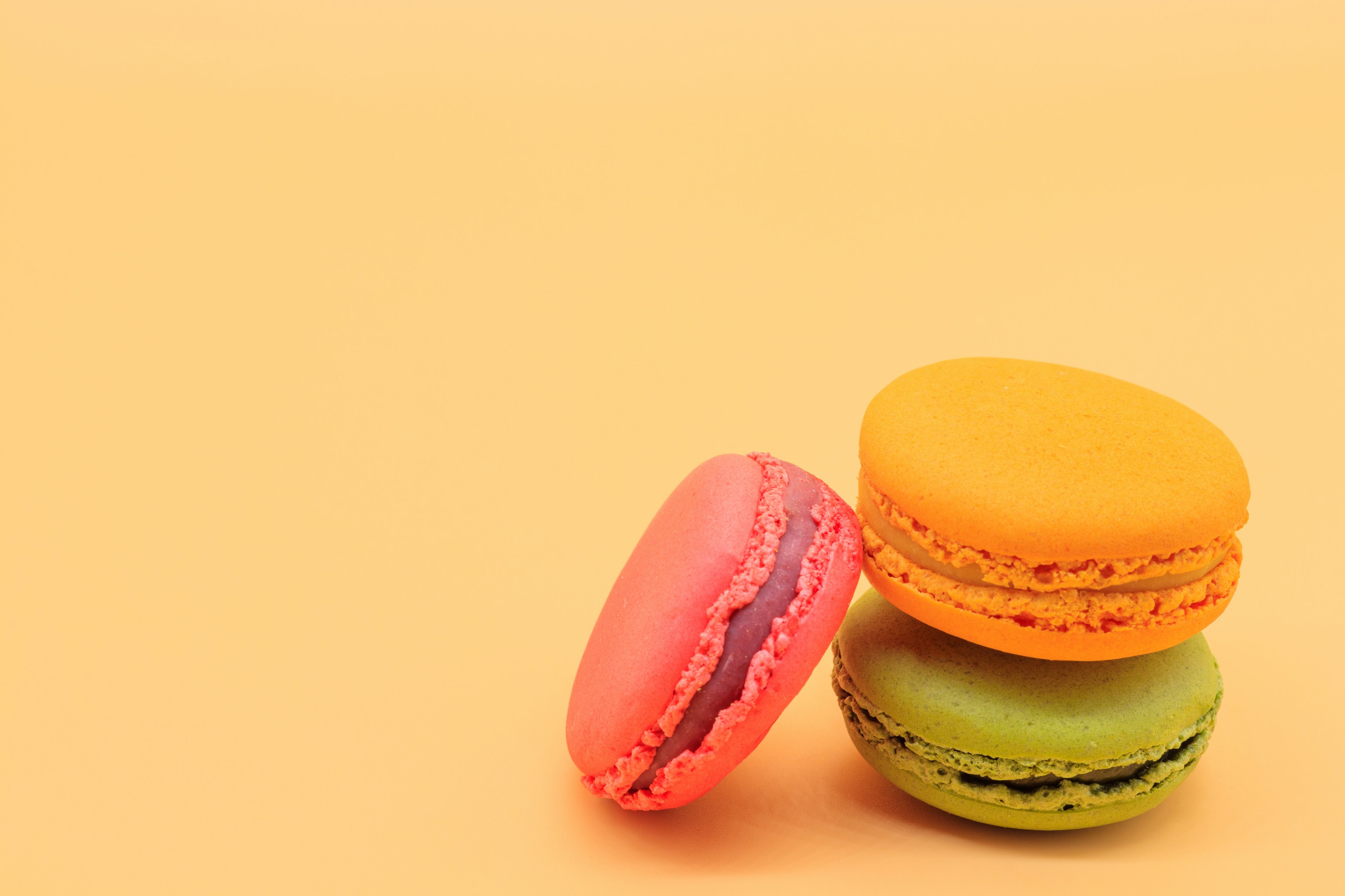 Trois macarons orange, vert et rose empilés sur un fond jaune