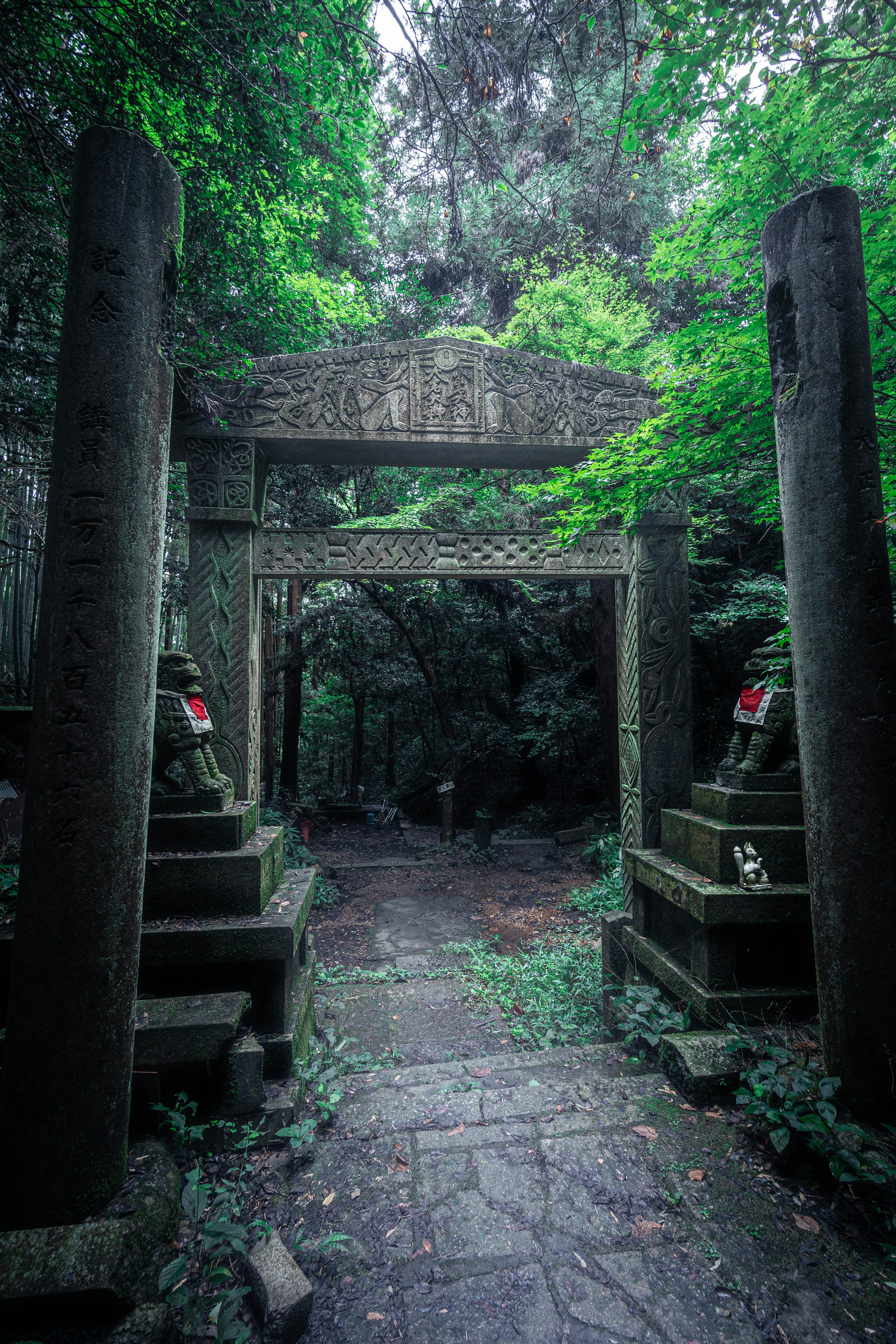 緑に覆われた石の鳥居と古い石の彫刻のある神秘的な小道