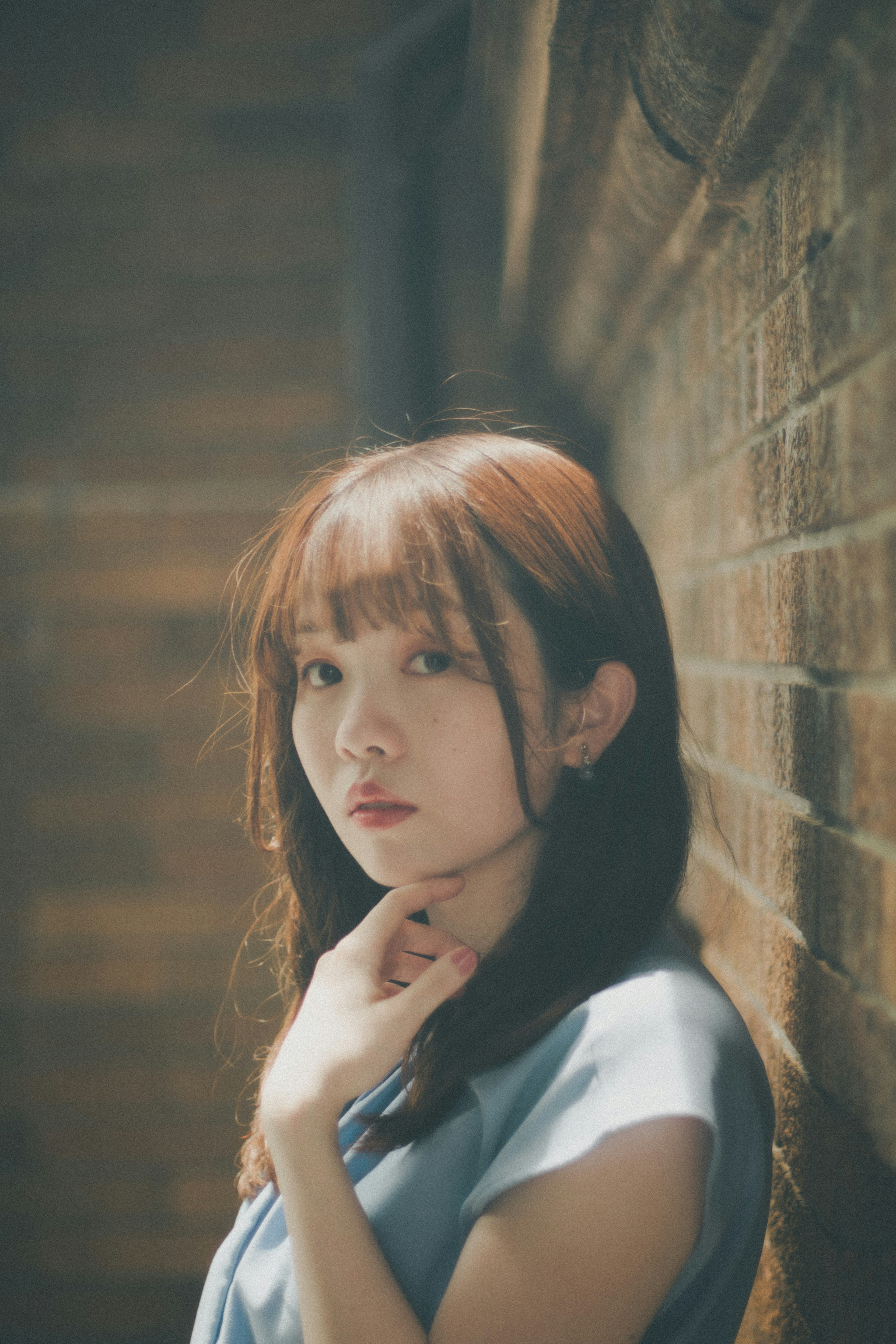 Portrait of a woman standing against a wall with soft lighting and a contemplative expression