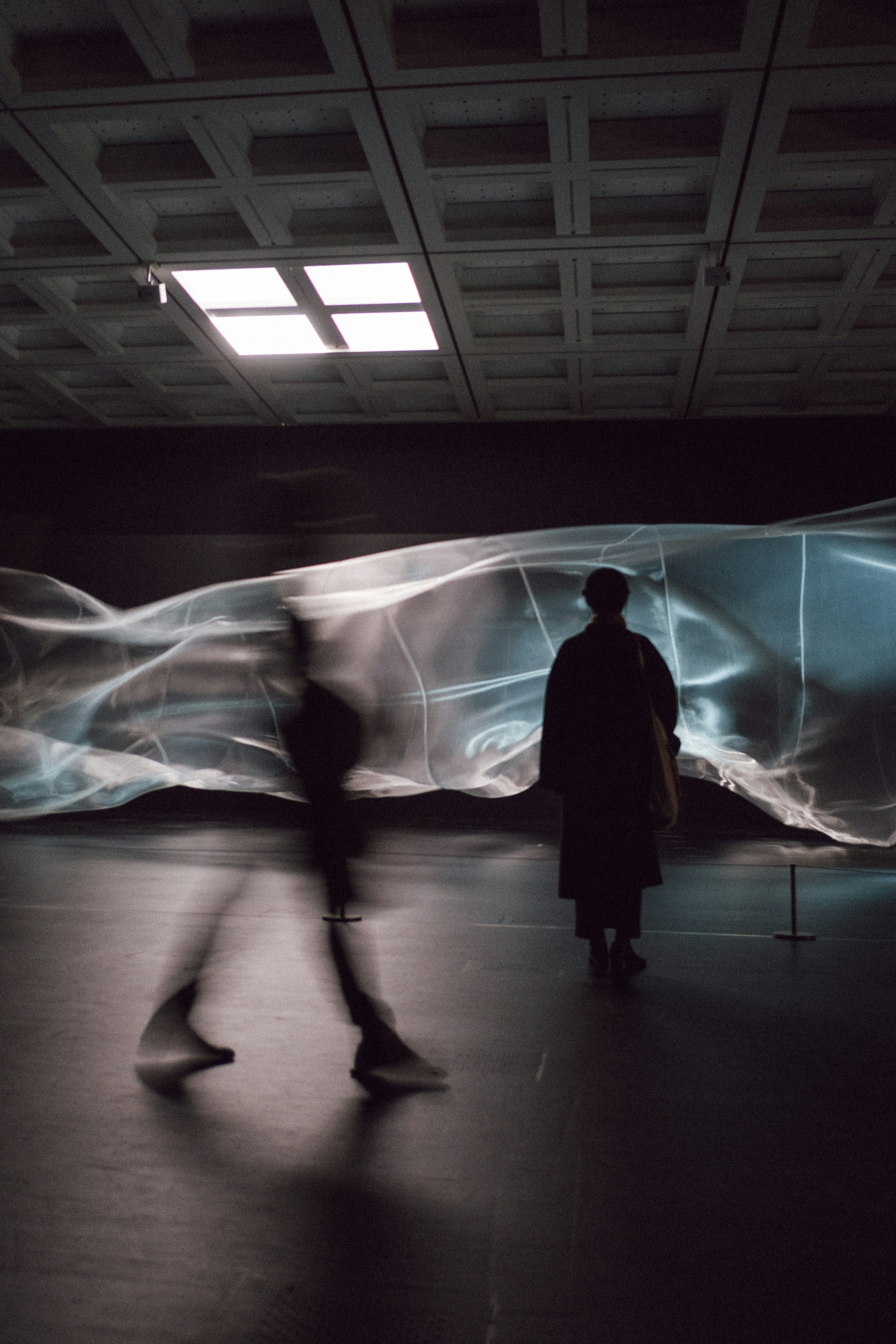 Silhouettes de personnes marchant devant un tissu translucide éclairé par une lumière bleue