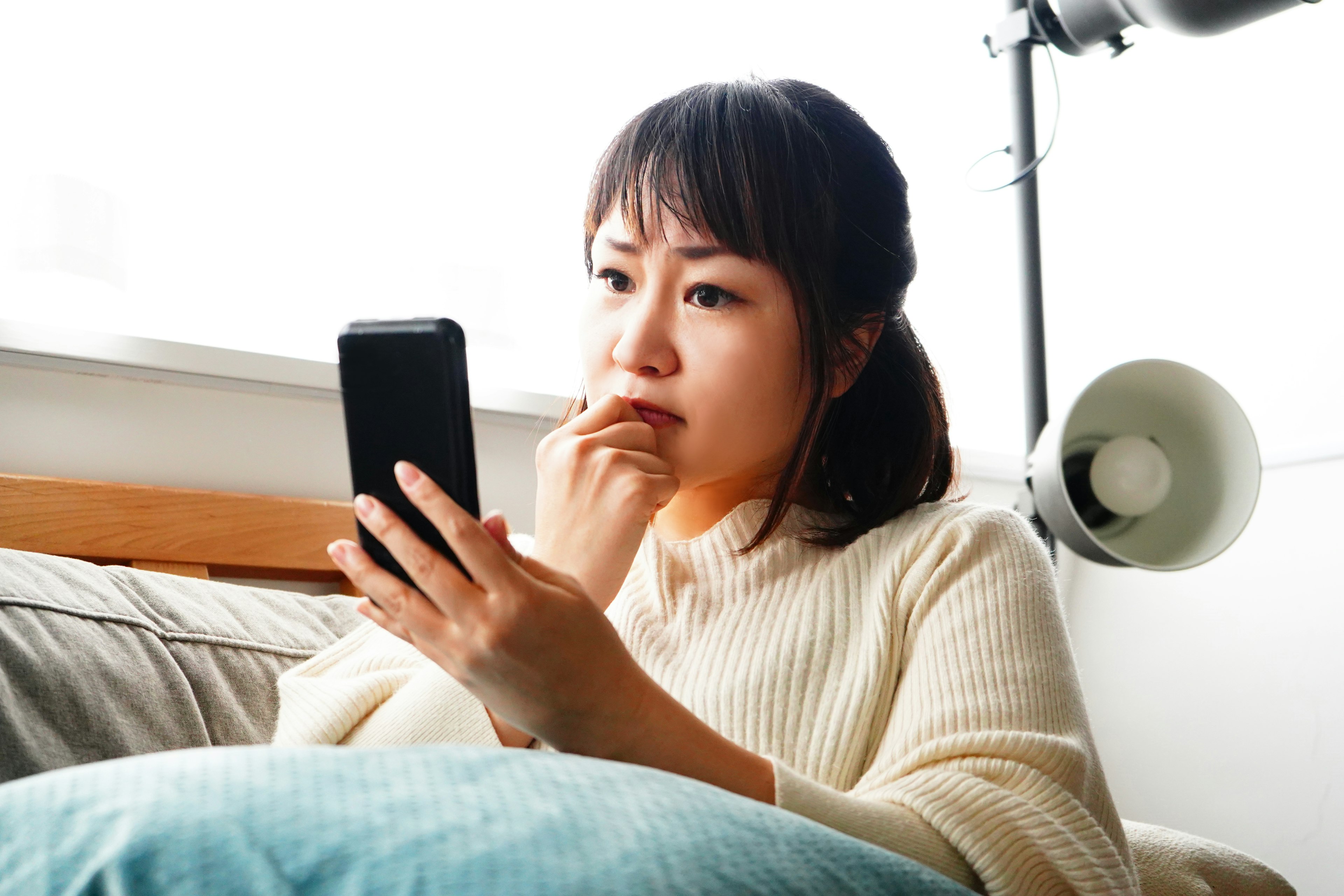 A woman looking at her smartphone wearing a white sweater sitting on a sofa