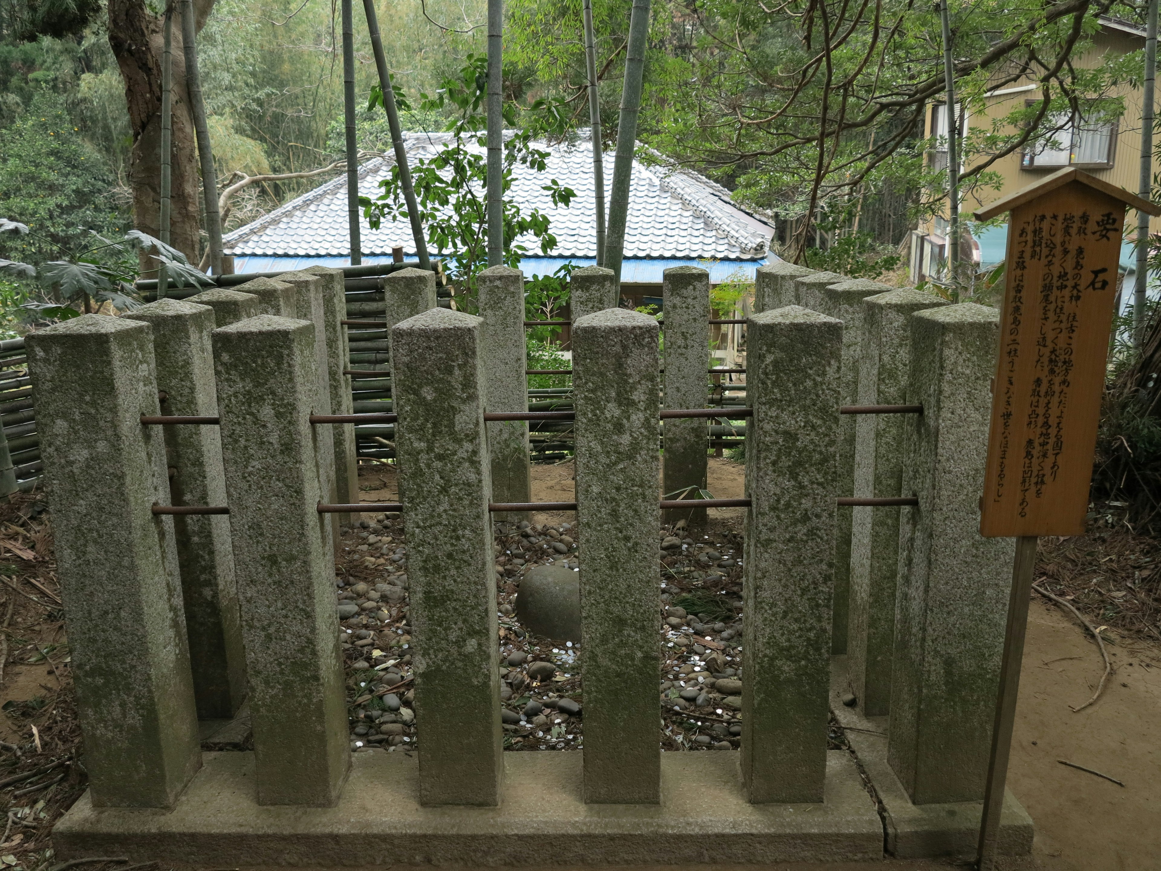 Primer plano de una estructura que combina columnas de piedra y varillas de hierro rodeadas de árboles