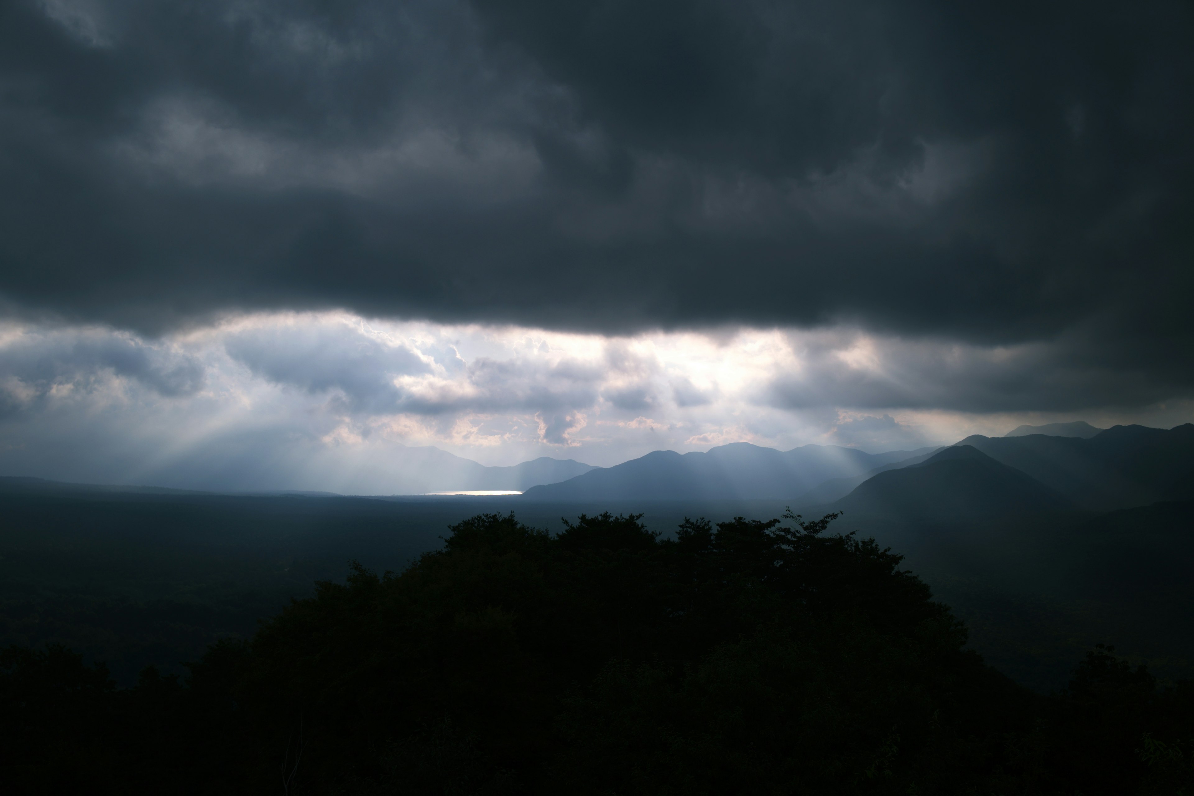 Silhouette di montagne sotto nuvole scure con raggi di luce che filtrano