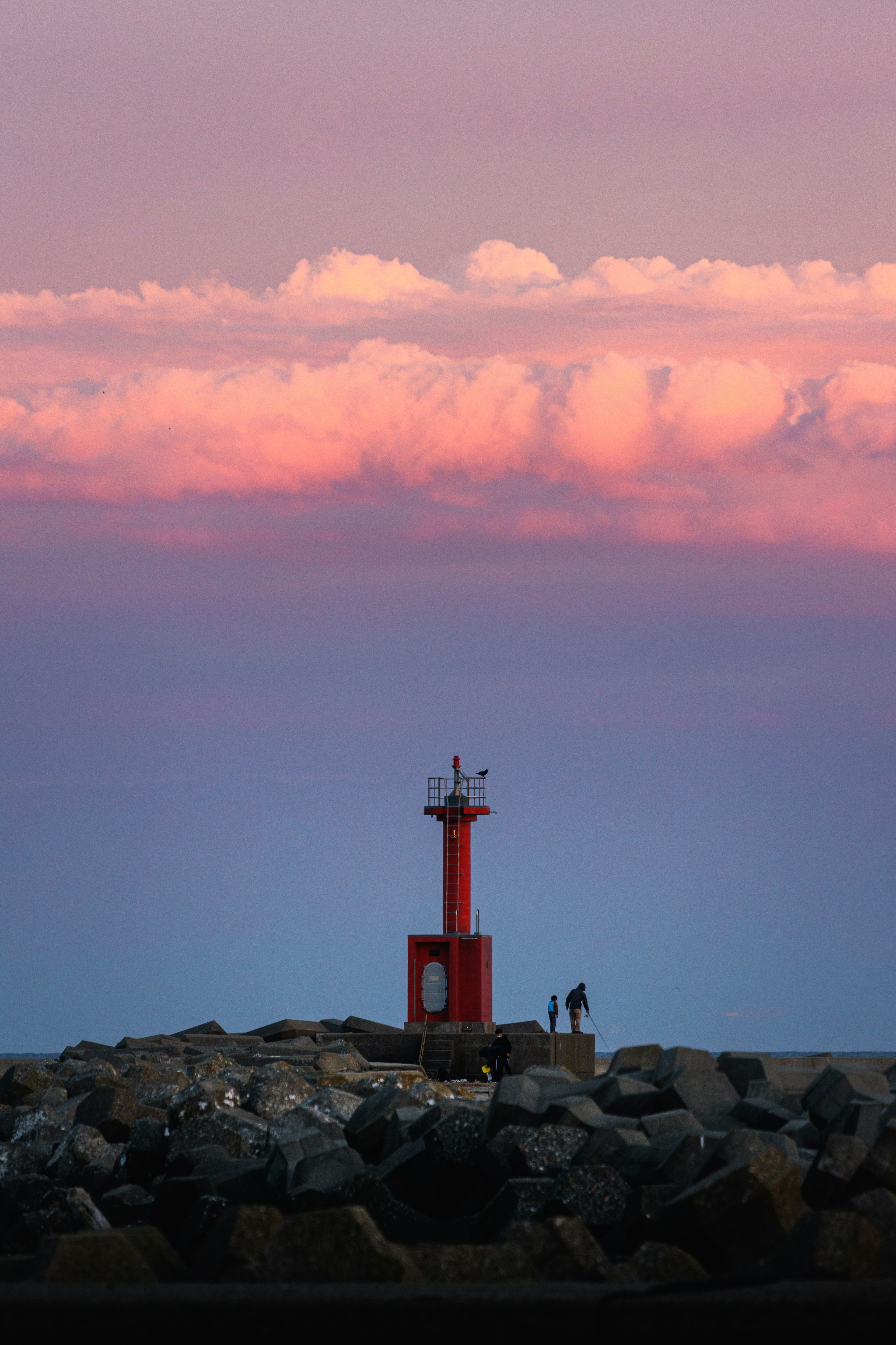 Red lighthouse against a sunset sky with clouds and two figures