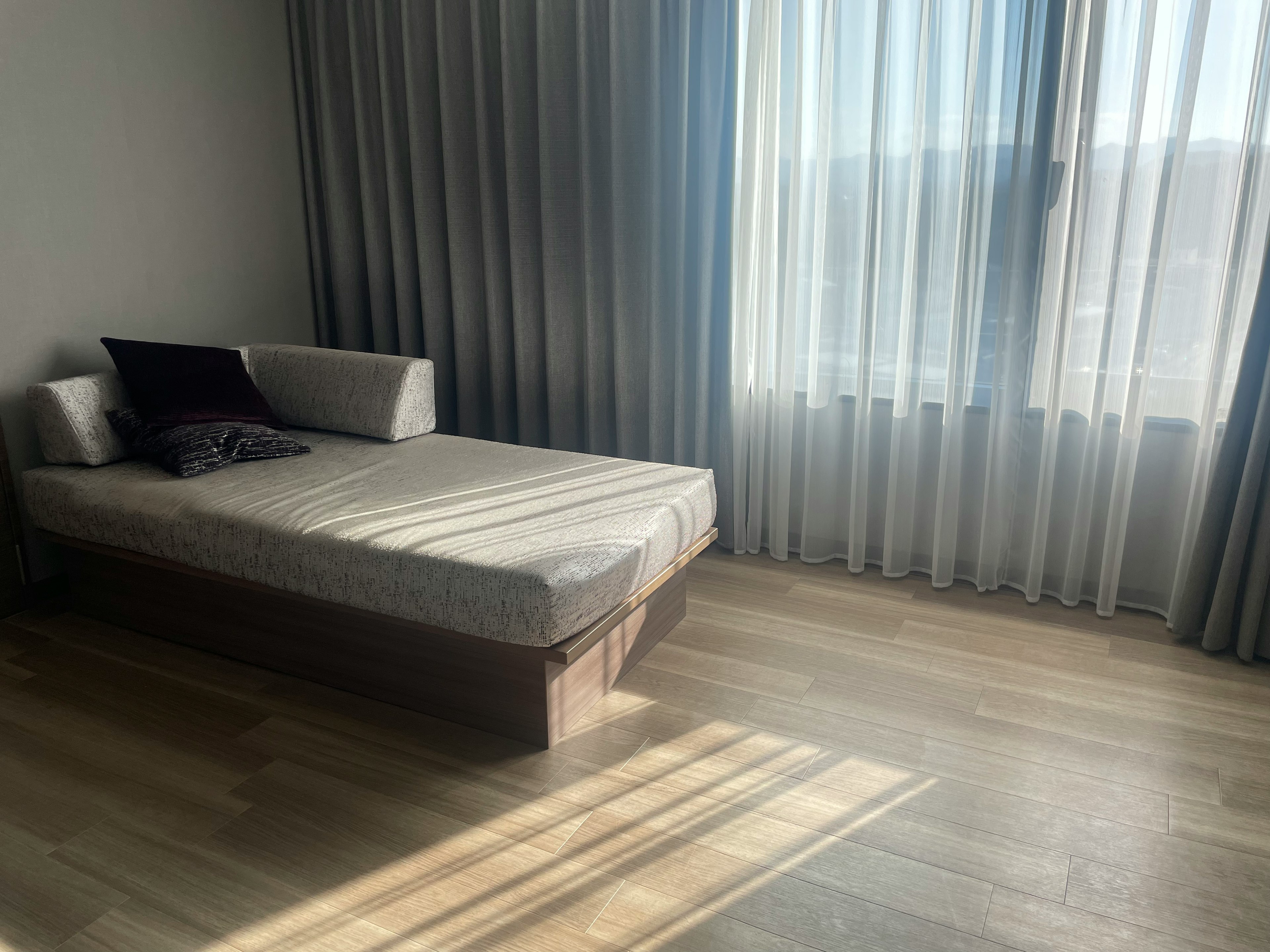 Habitación minimalista iluminada con una cama de sábanas blancas y un cojín Luz suave del sol a través de cortinas transparentes