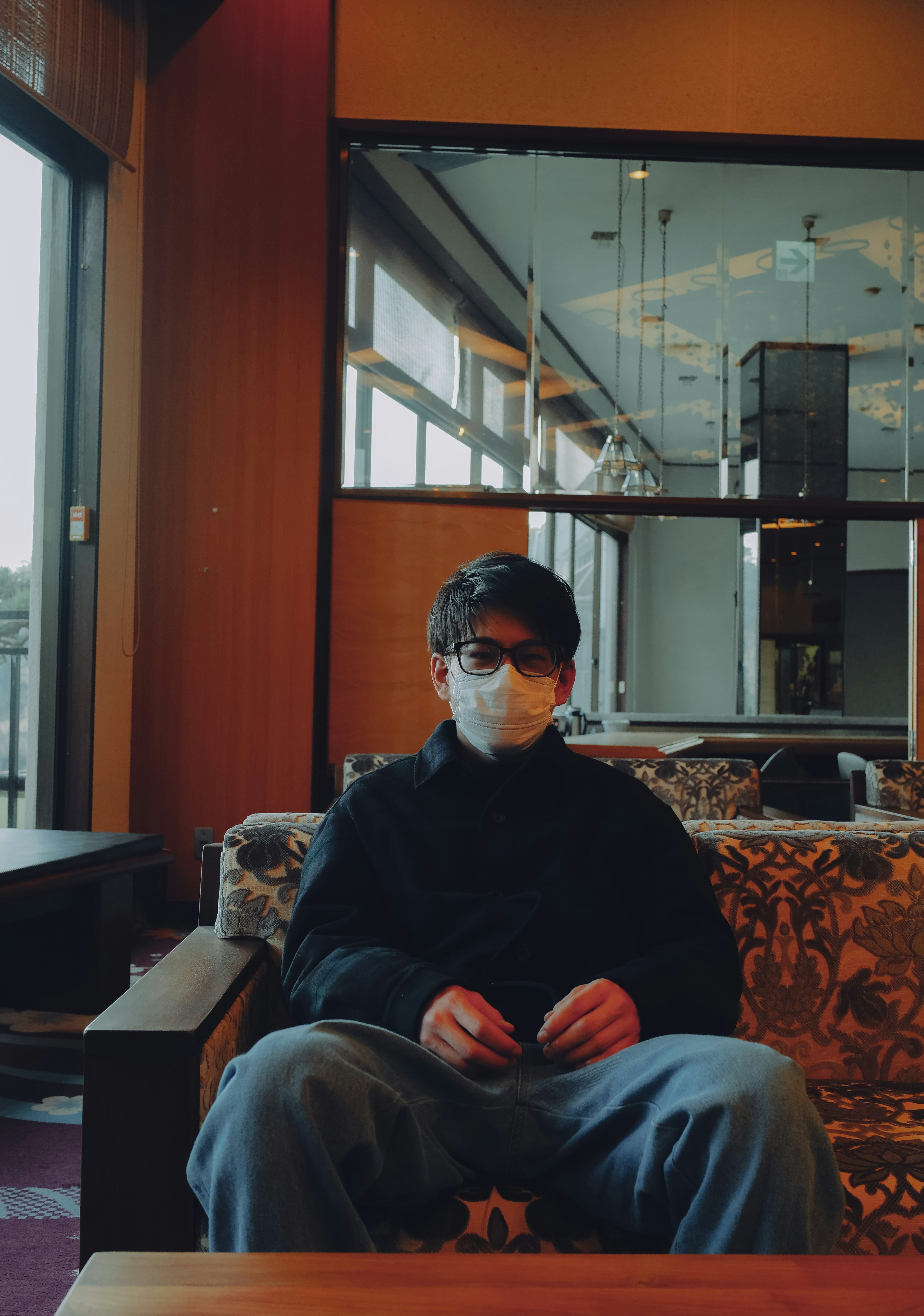 A man wearing a mask sitting on a sofa with visible interior background details