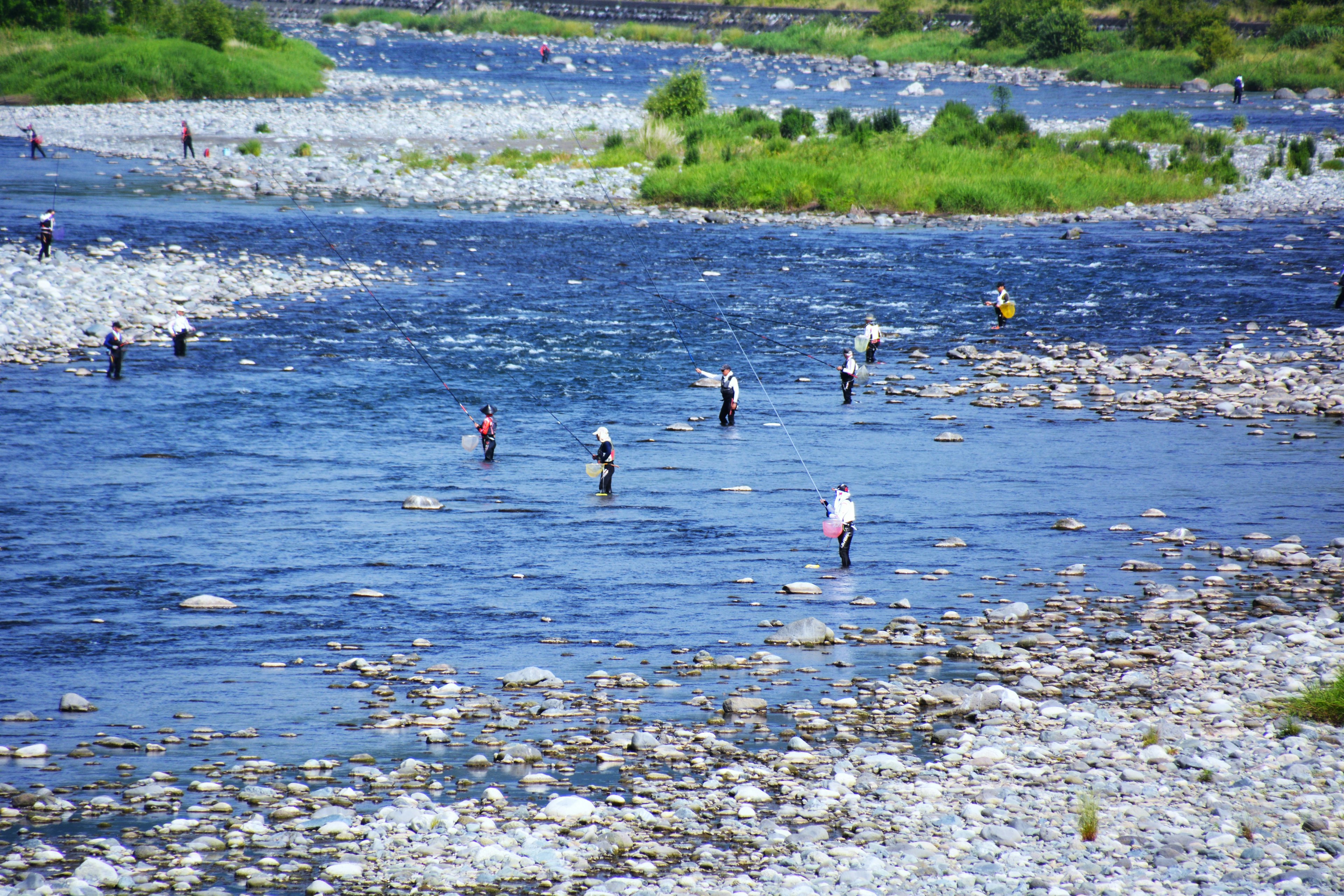 Orang-orang memancing di sungai dikelilingi tepi berbatu dan vegetasi hijau