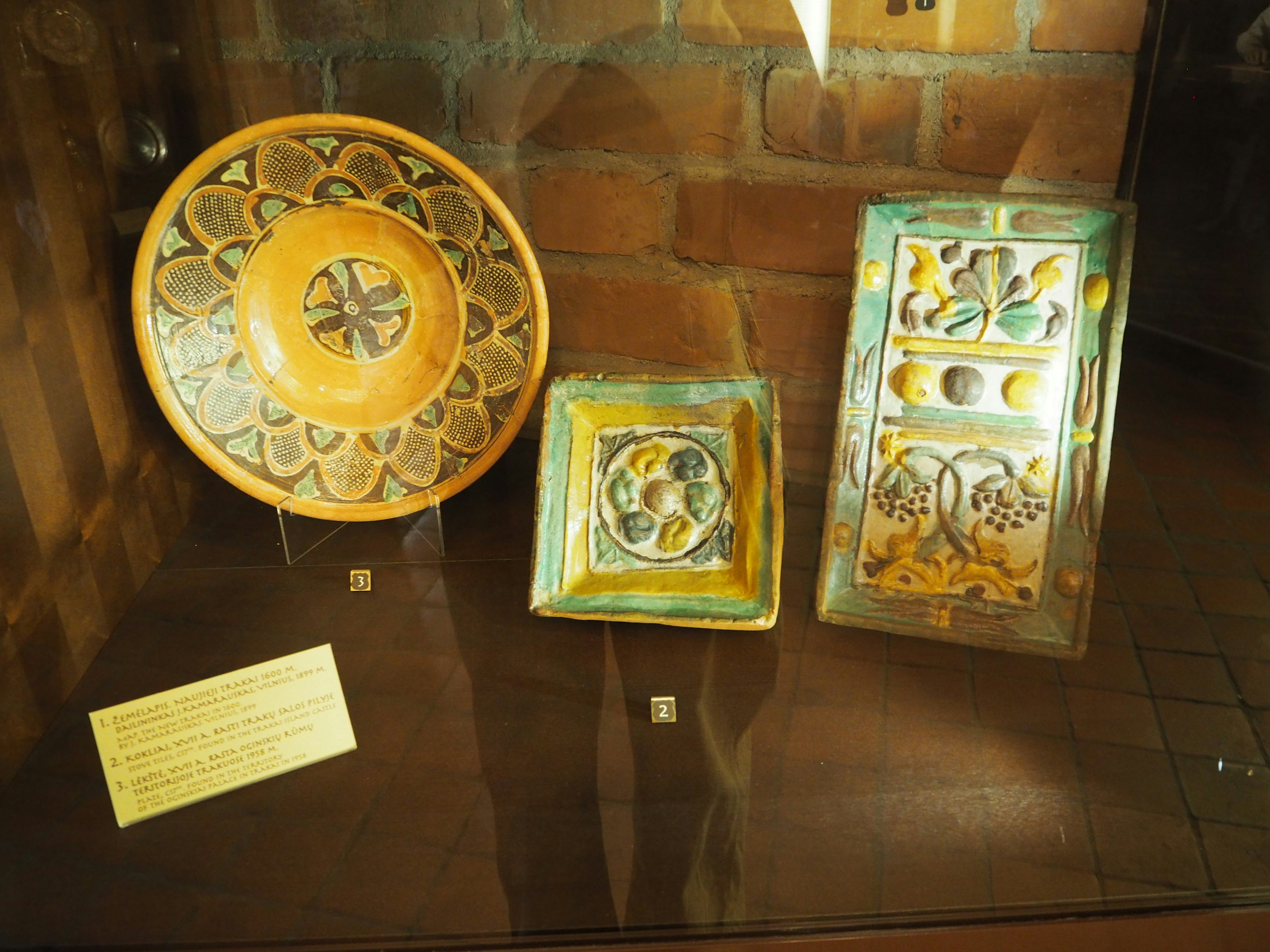 Trois pièces de poterie ancienne avec des décorations complexes exposées dans une vitrine en verre