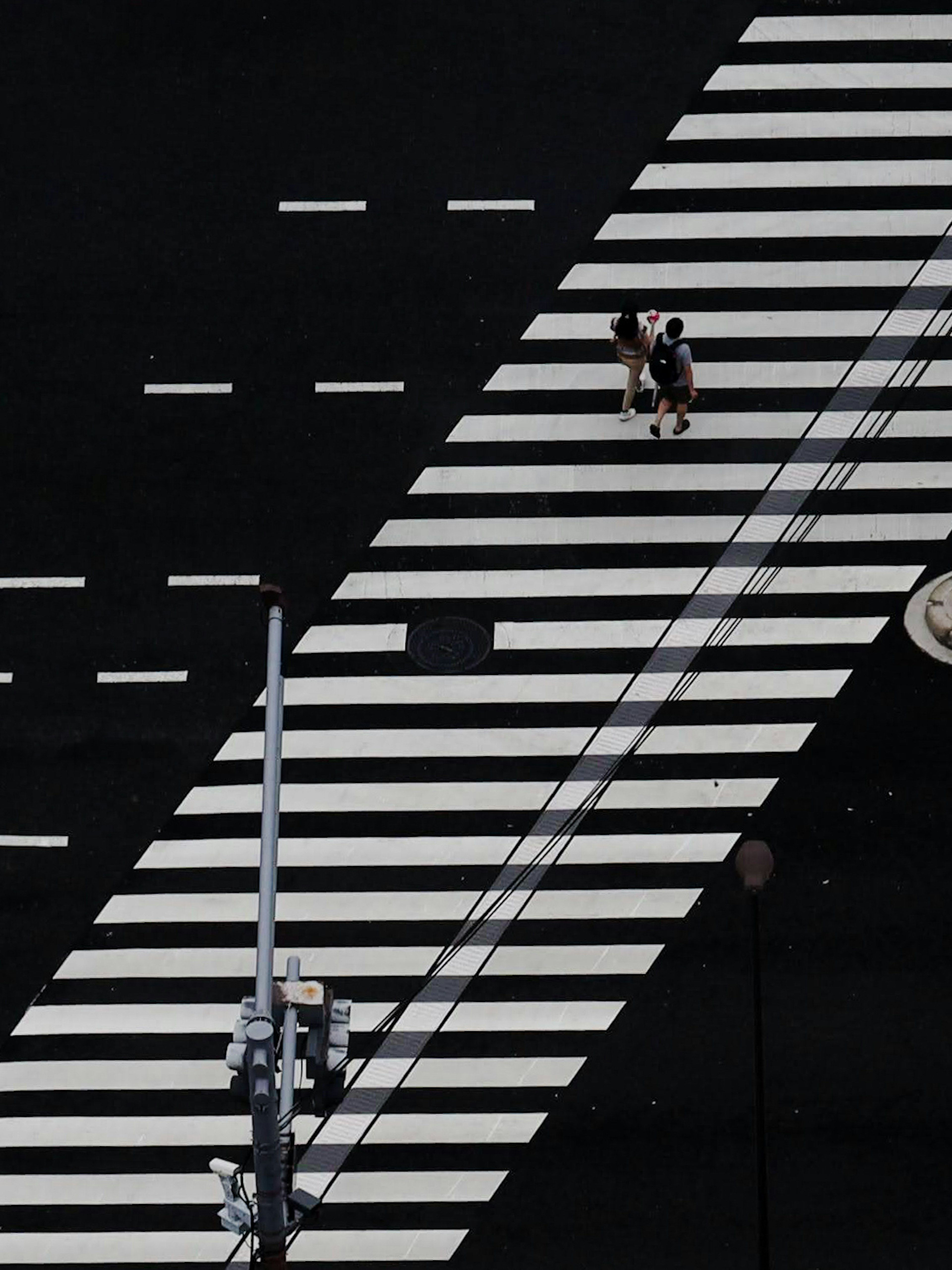 Aerial view of a pedestrian crossing with a person walking and a traffic pole