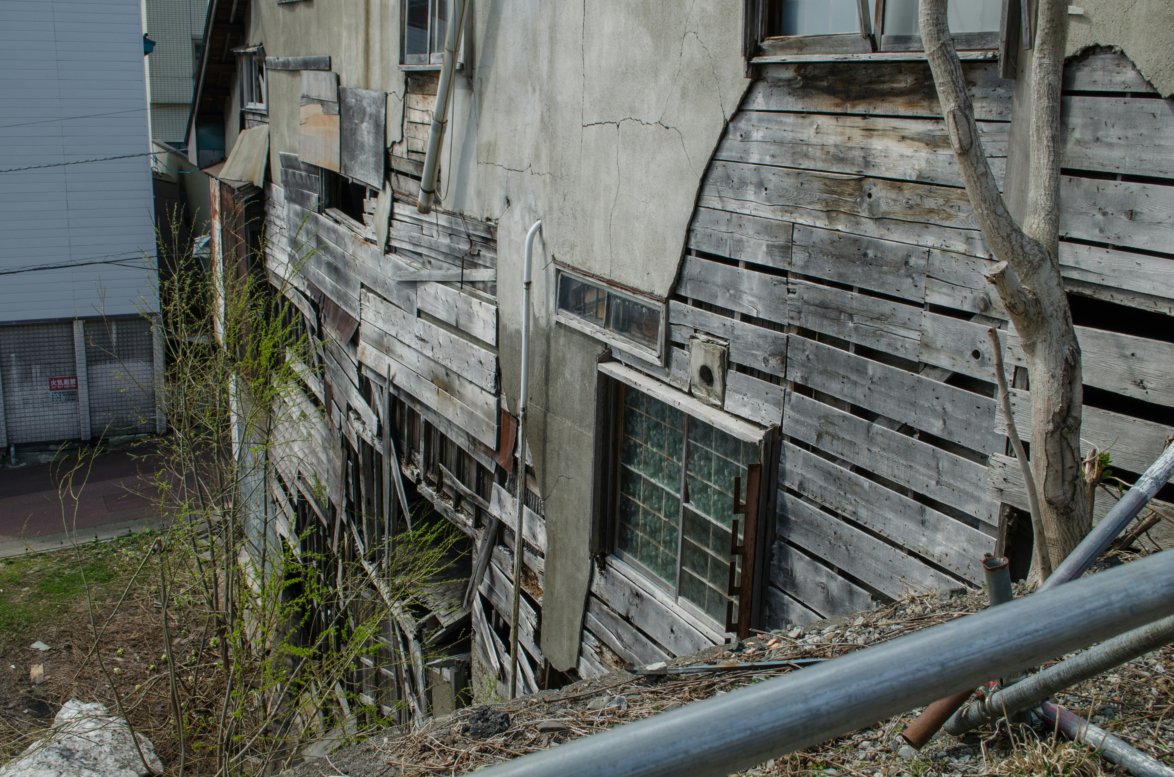 Bild zeigt die Seite eines alten Holzhauses mit abblätternden Wänden und einem sichtbaren Fenster