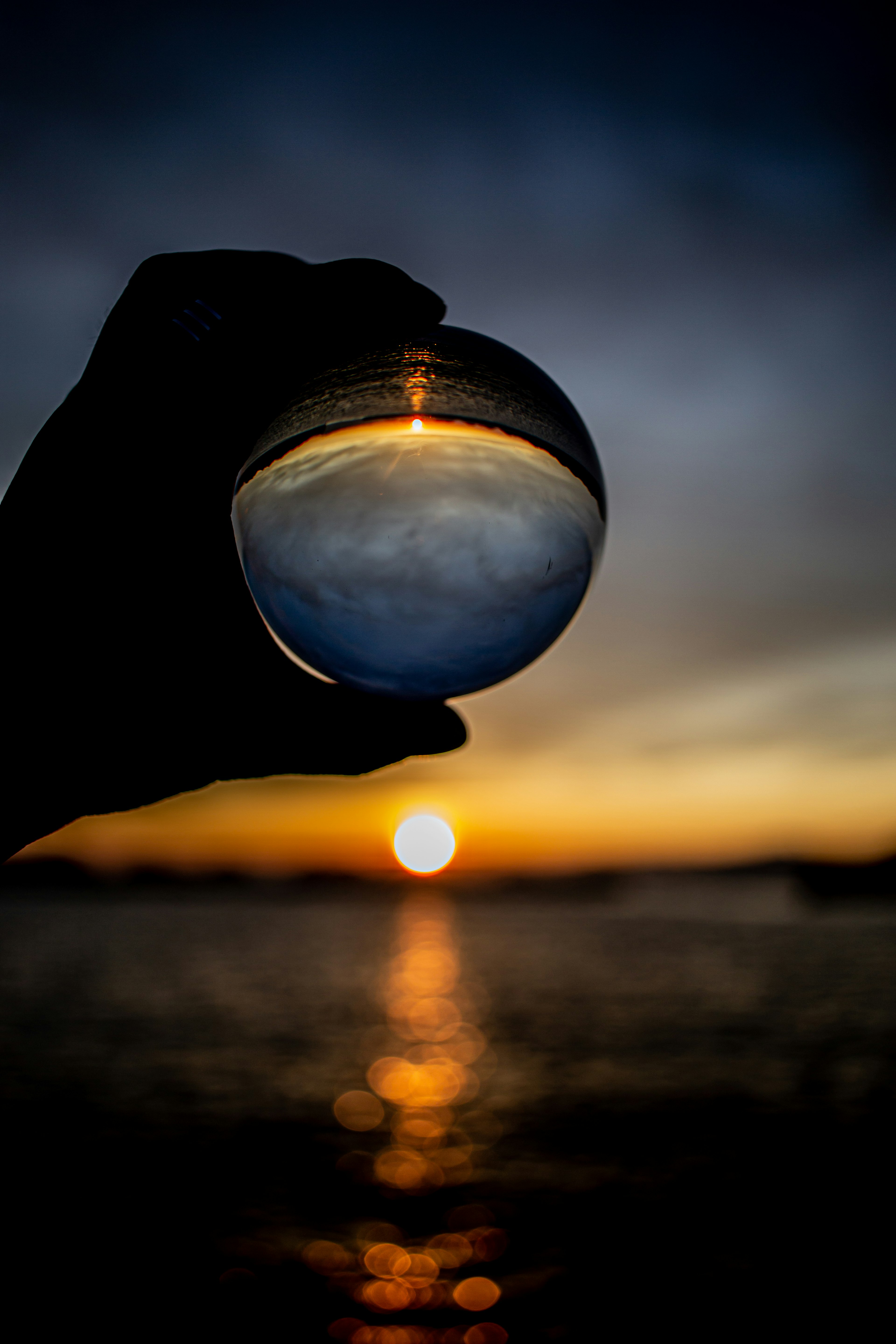 Vista del tramonto e dell'oceano attraverso una sfera di cristallo tenuta in mano