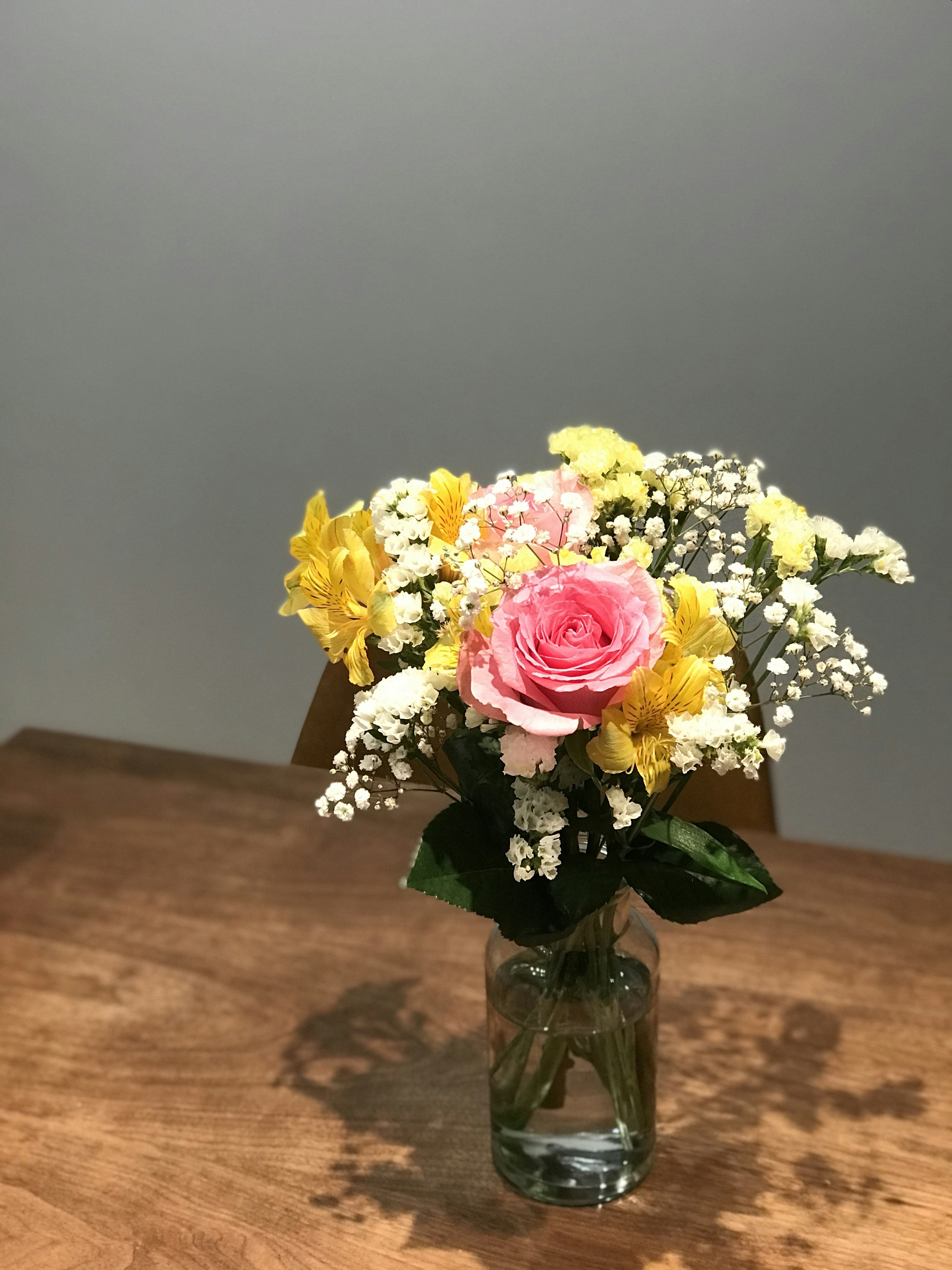 A bouquet of pink rose and yellow flowers in a glass vase