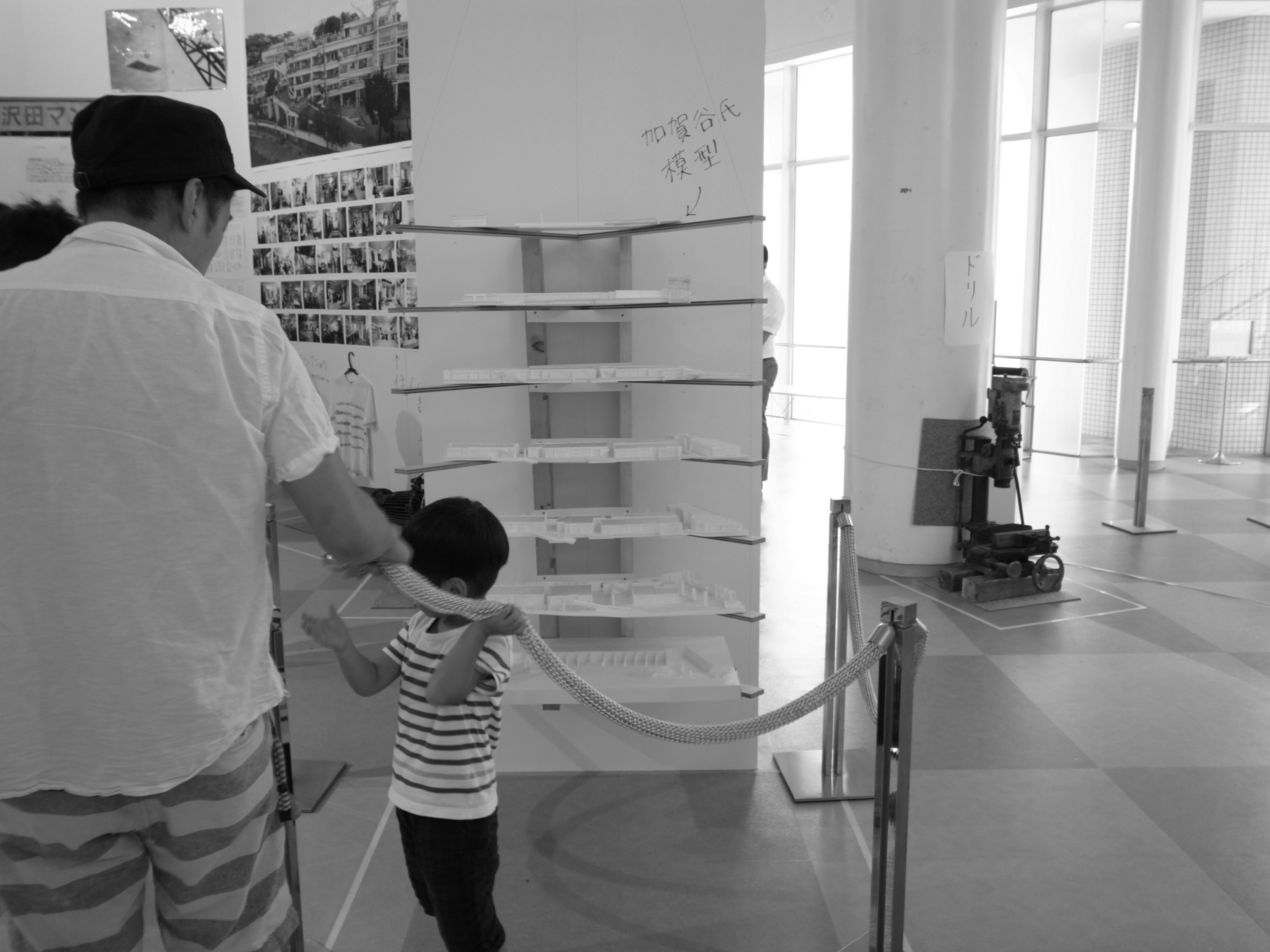 Black and white photo of a child and an adult holding a rope in an exhibition space