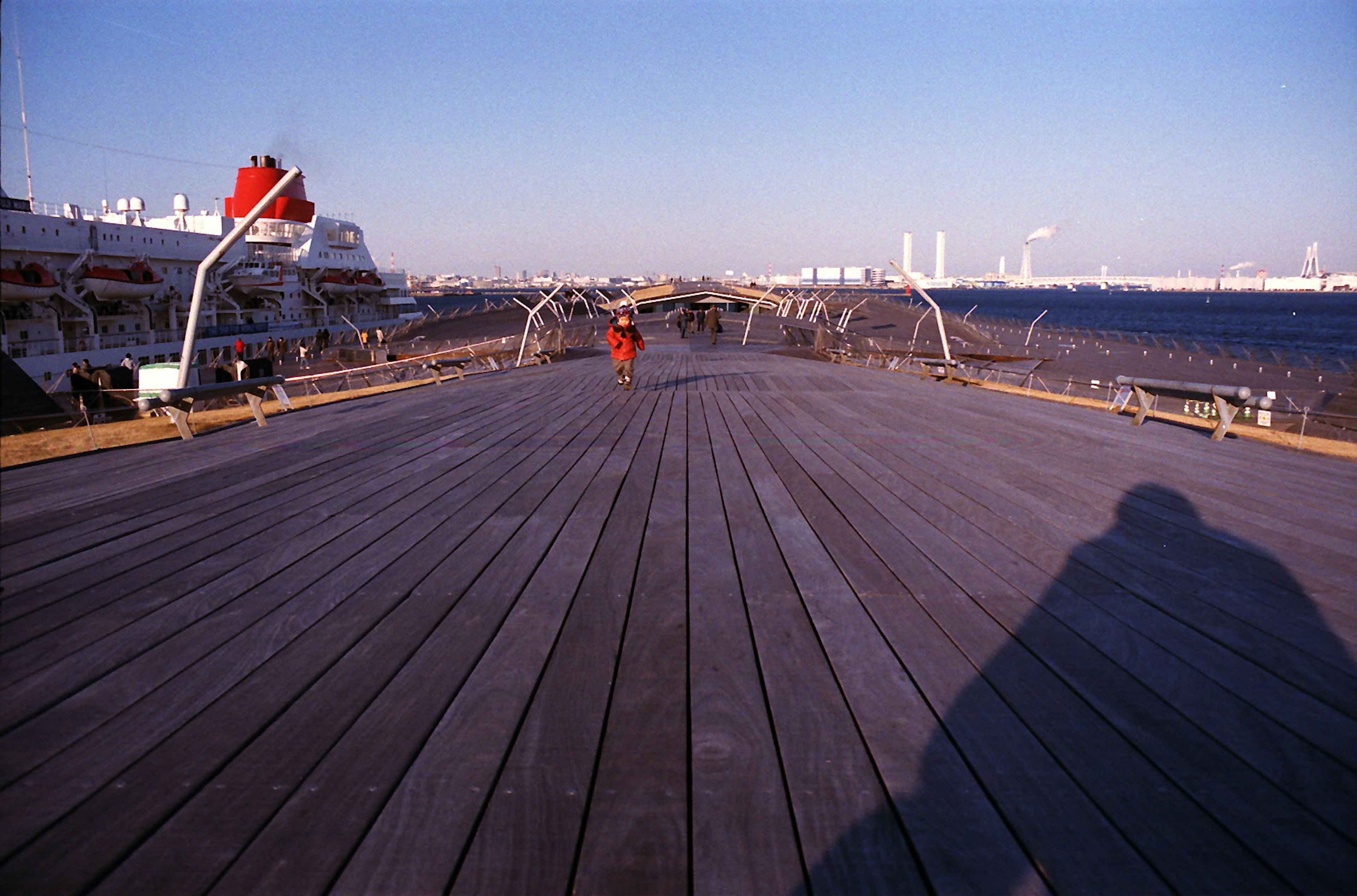 Eine Person steht auf einem Holzdeck am Meer unter einem blauen Himmel