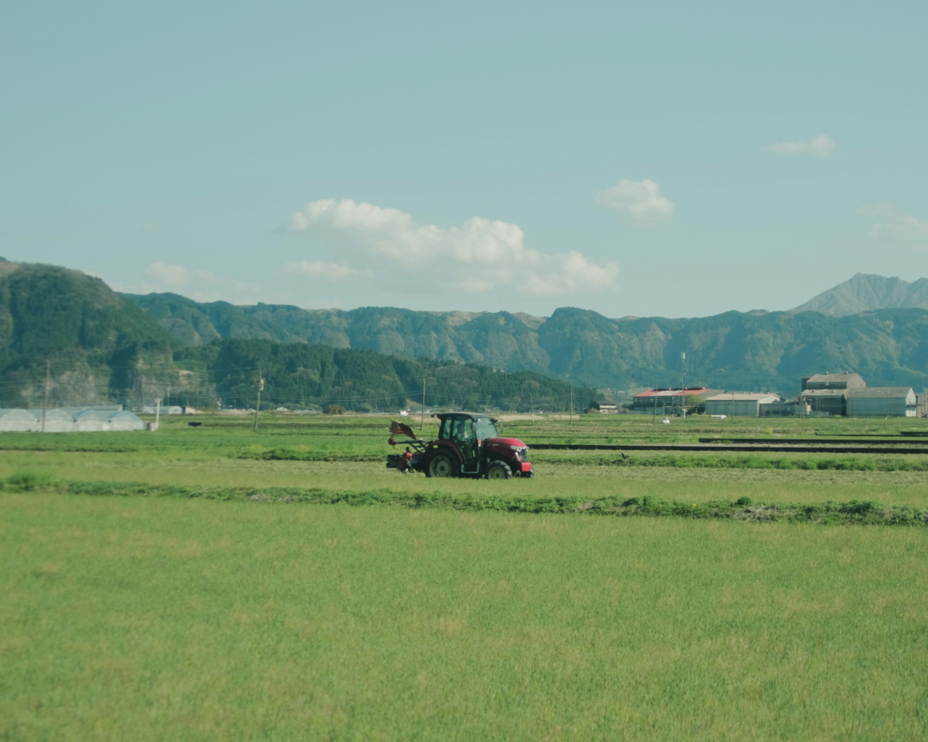 Tractor trabajando en un campo de arroz verde con montañas al fondo