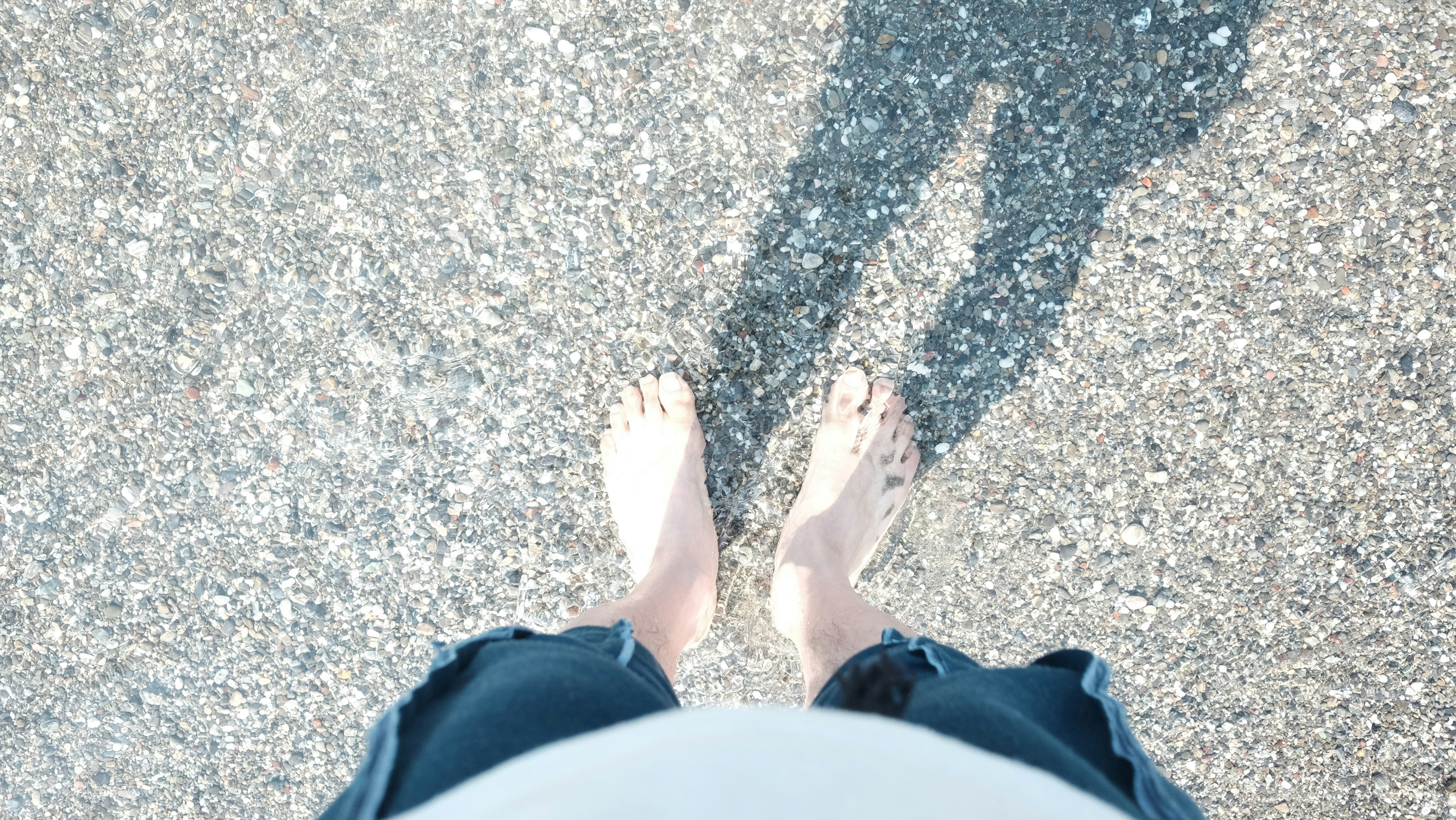 Bird's-eye view of a person standing barefoot with shadow on the ground