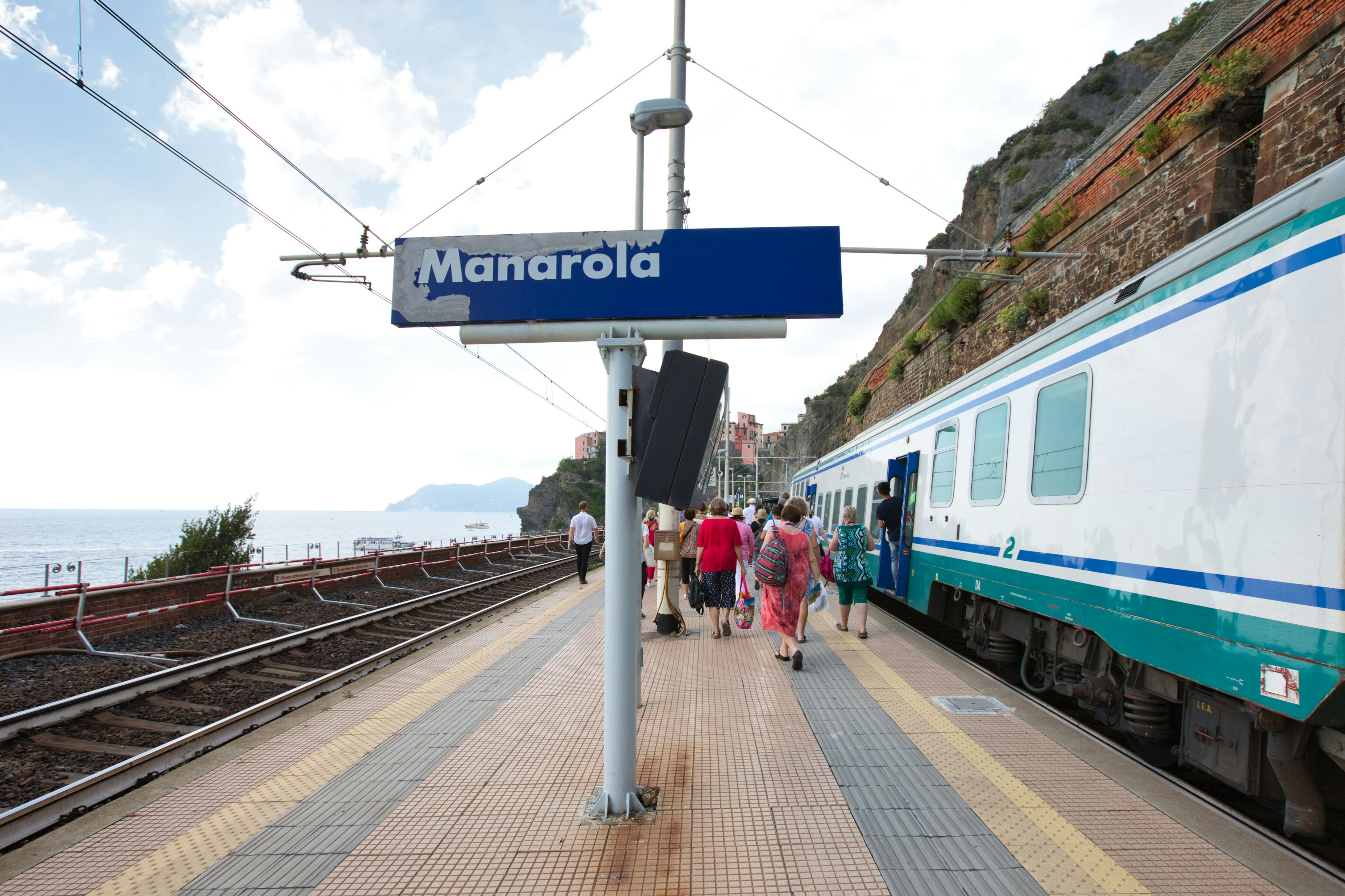 Passengers at Manarola train station with a train and coastal scenery