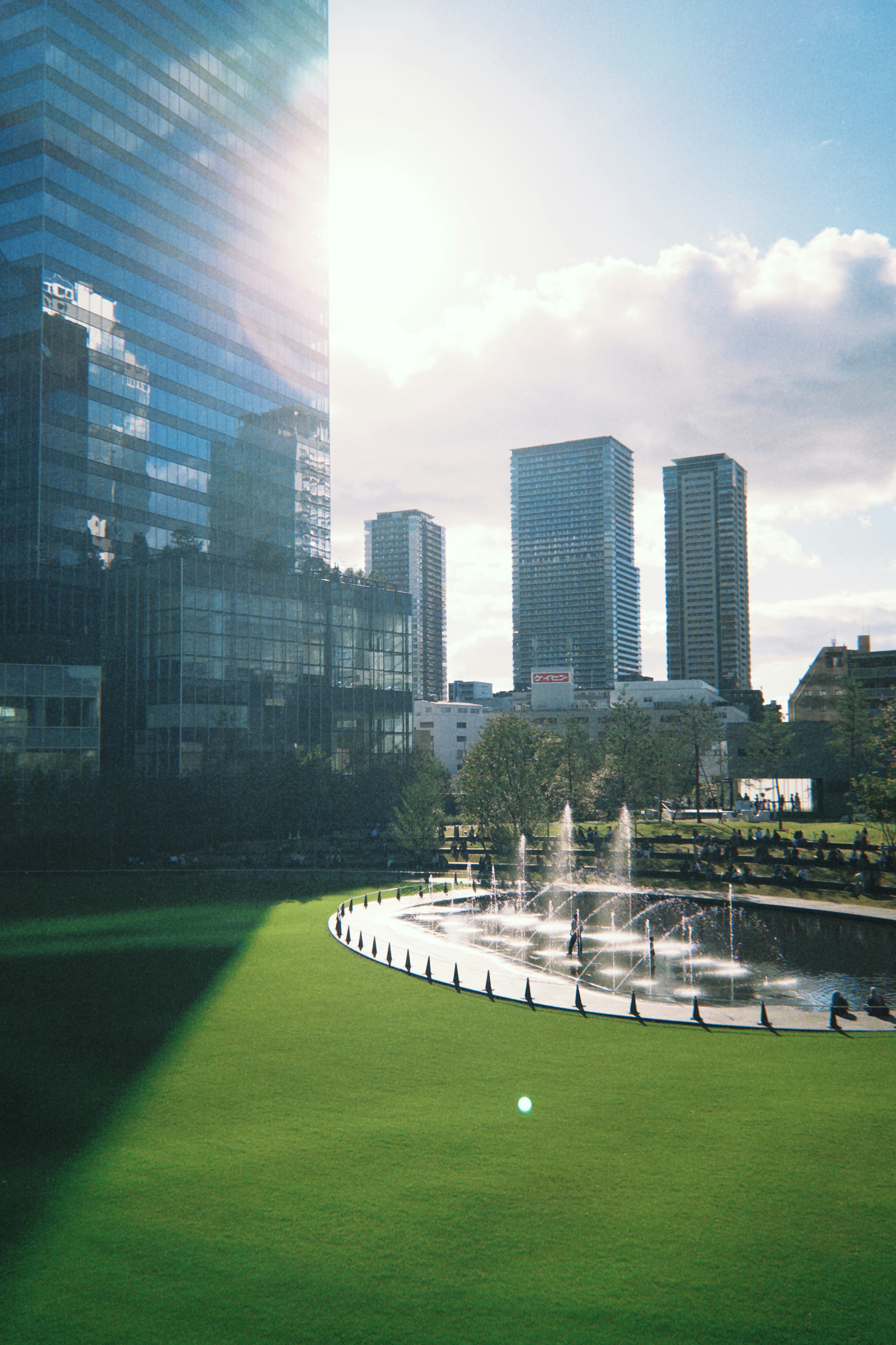 Urban park with tall buildings and a fountain sunlight reflecting off glass