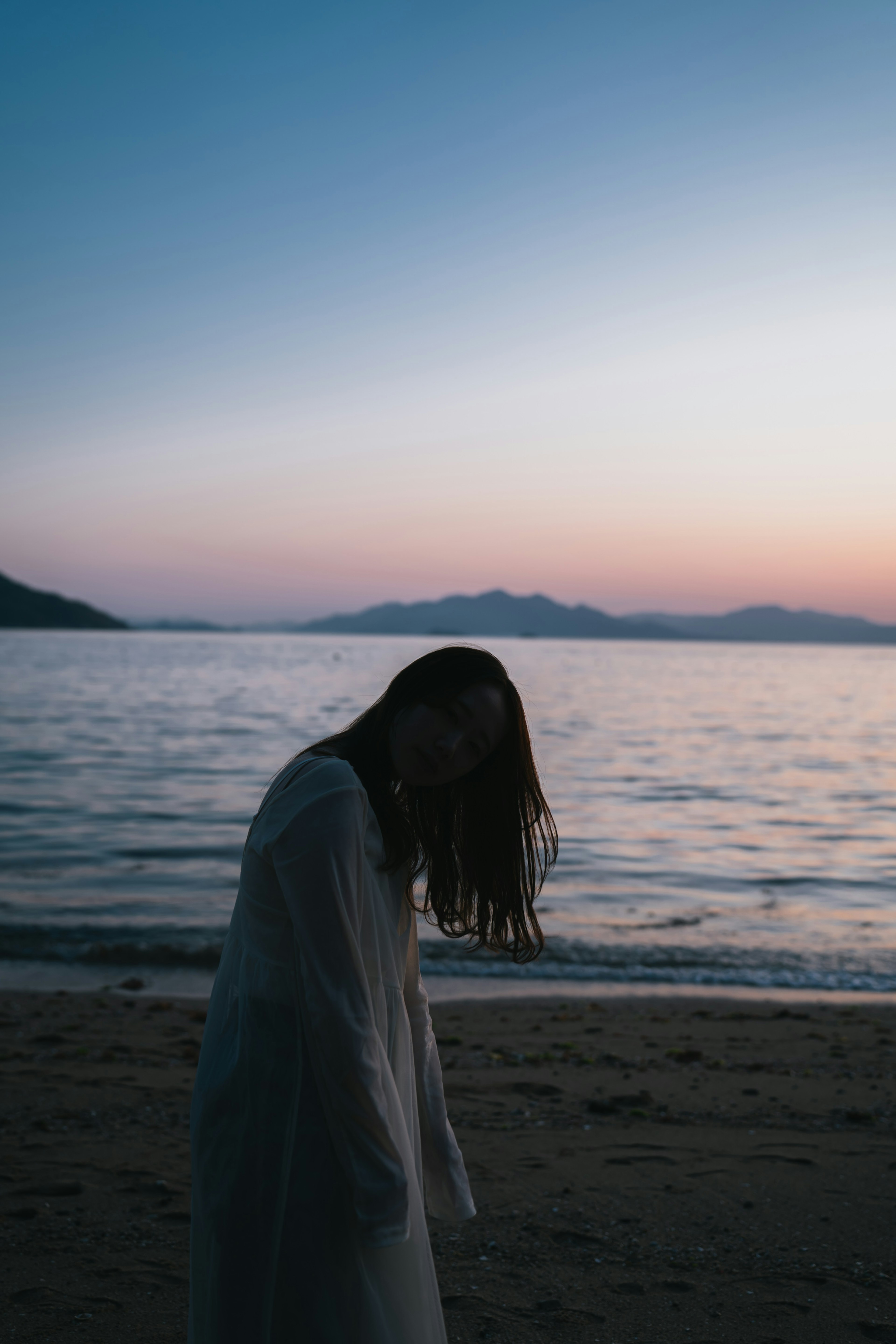 海灘上長髮女性的輪廓在日落時分與平靜的海洋和山脈