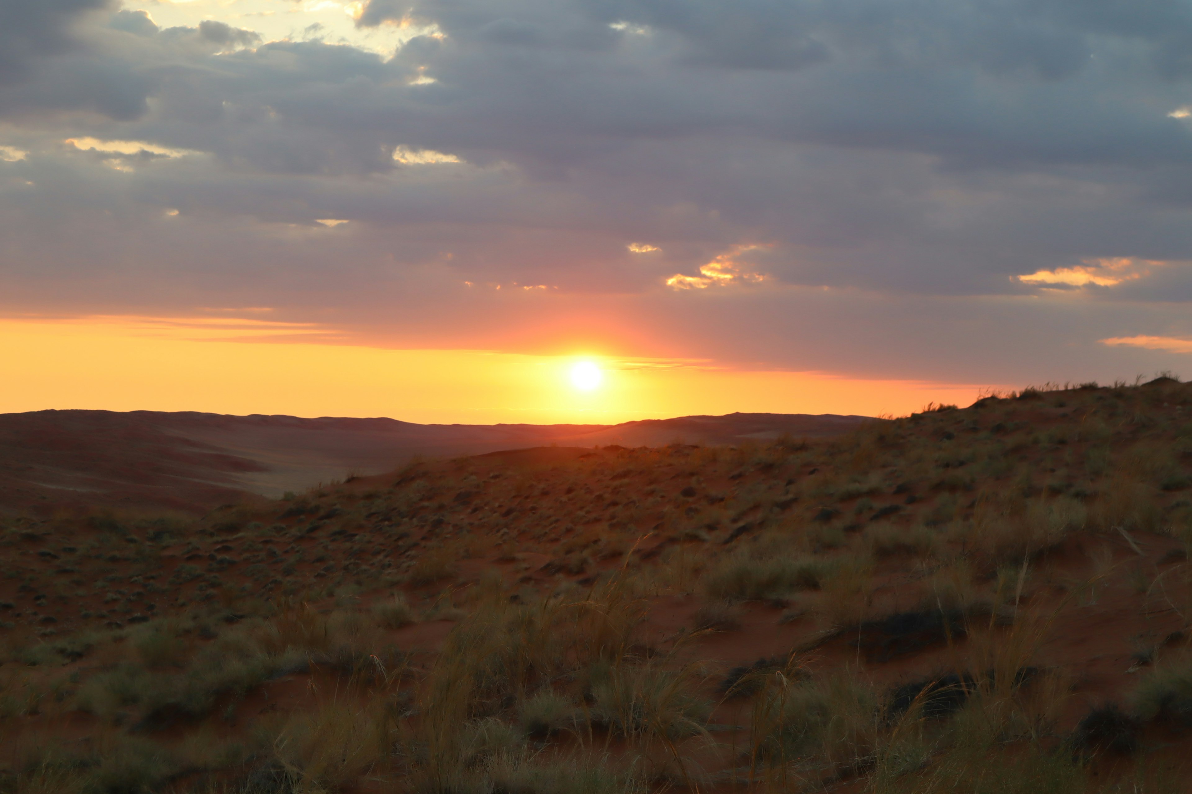 Sonnenuntergang über sanften Hügeln mit dramatischen Wolken