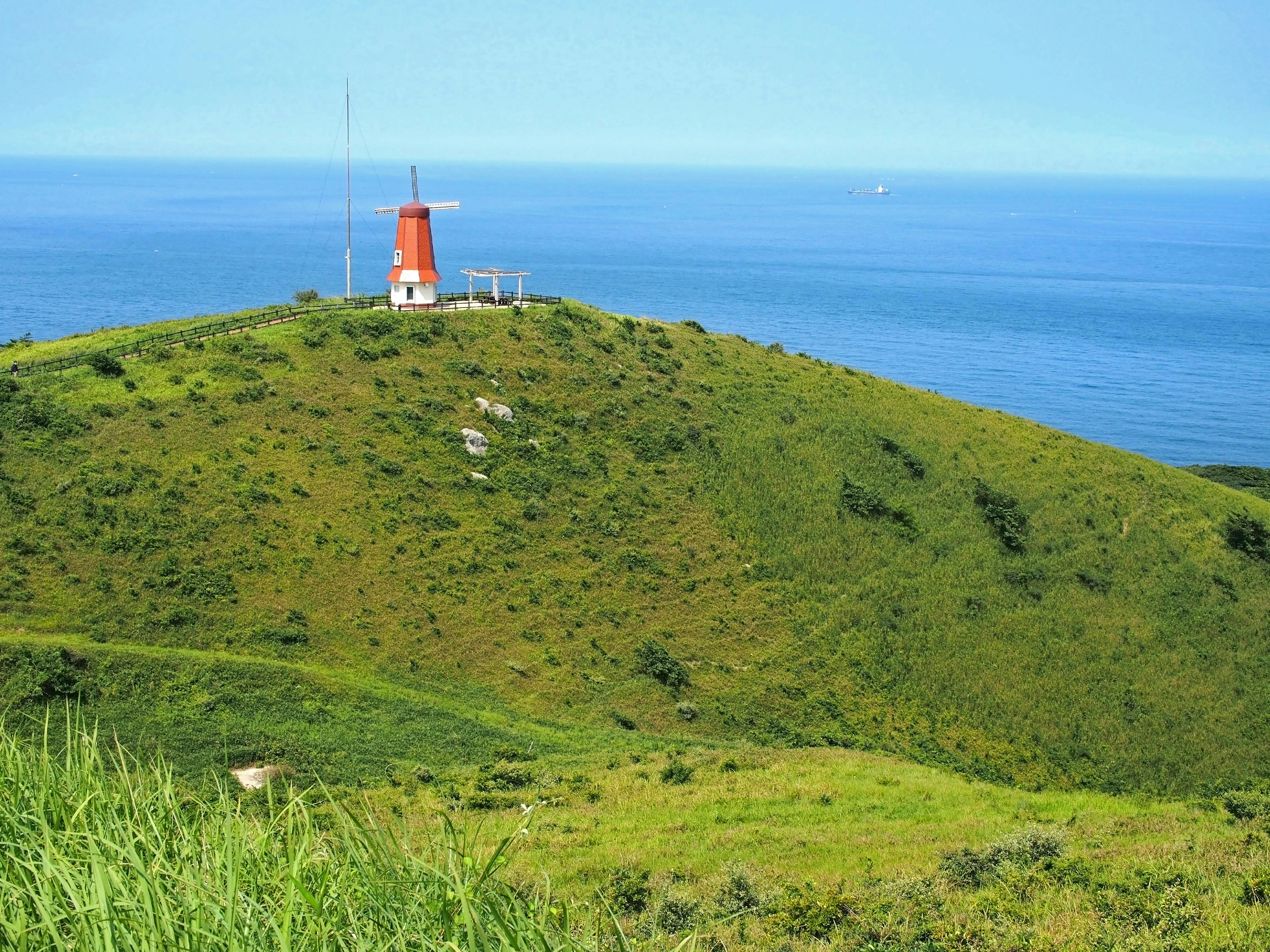 Red windmill on a green hill overlooking the blue sea