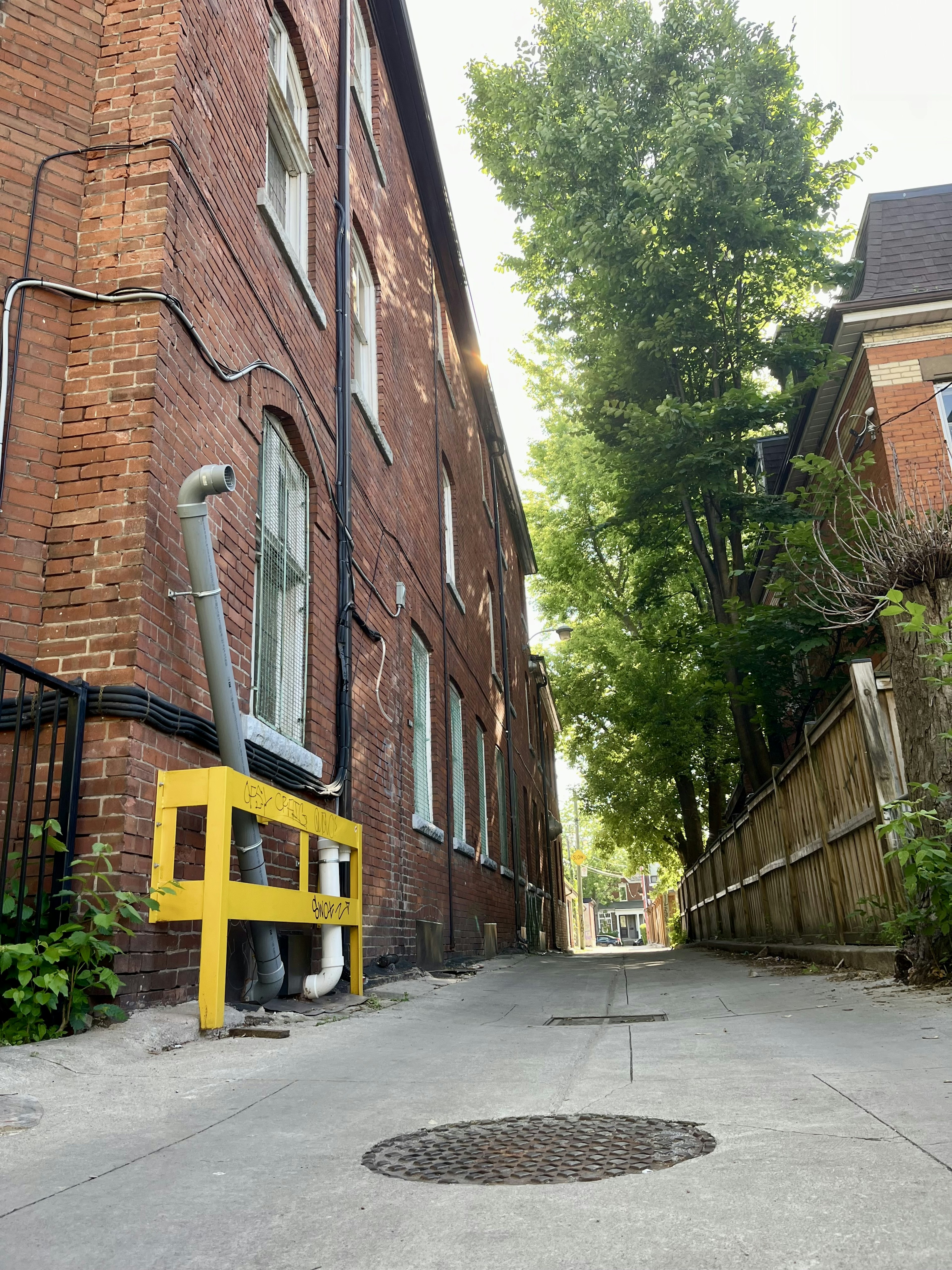 Narrow alleyway featuring red brick buildings and green trees