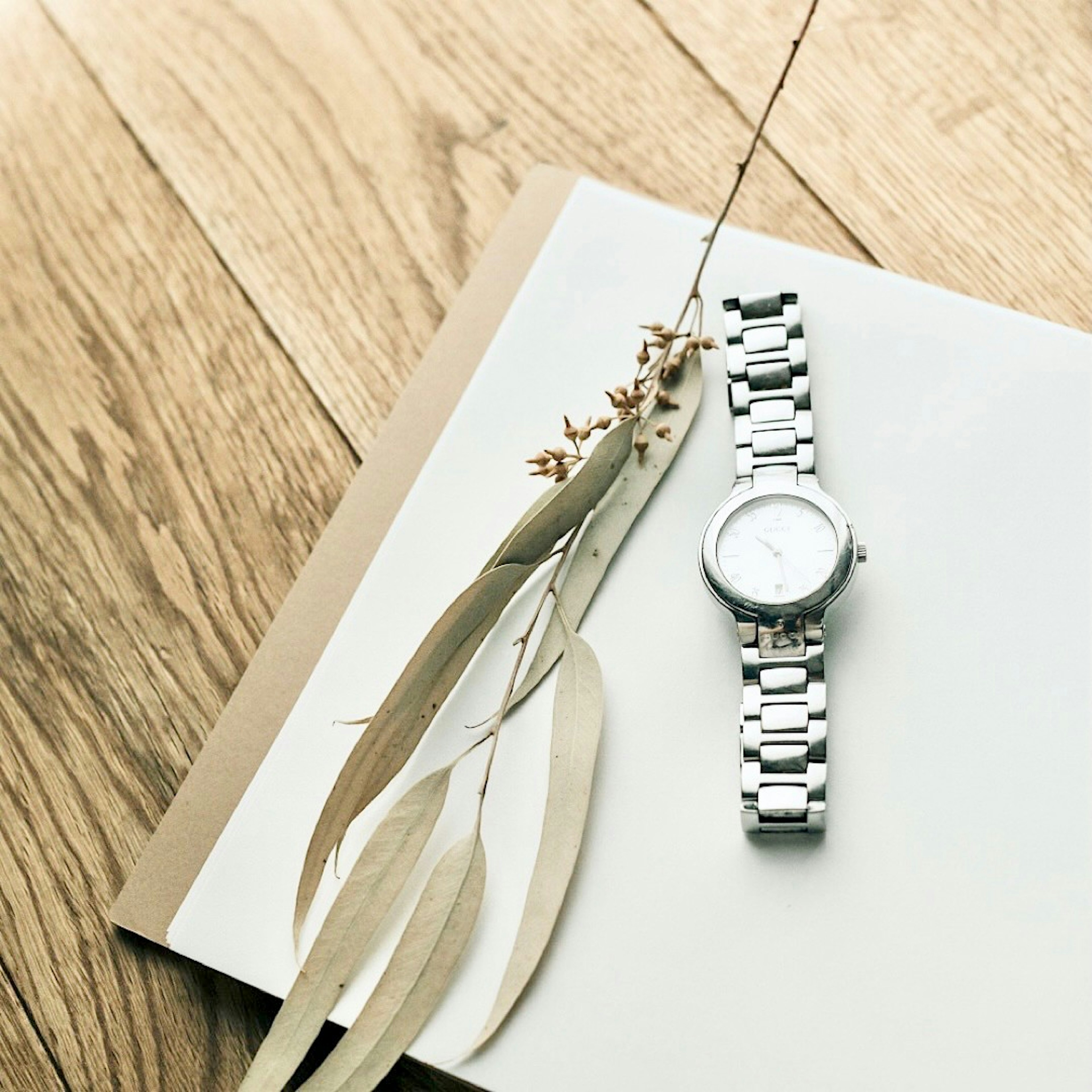 Reloj de plata y flores secas sobre un cuaderno en una mesa de madera