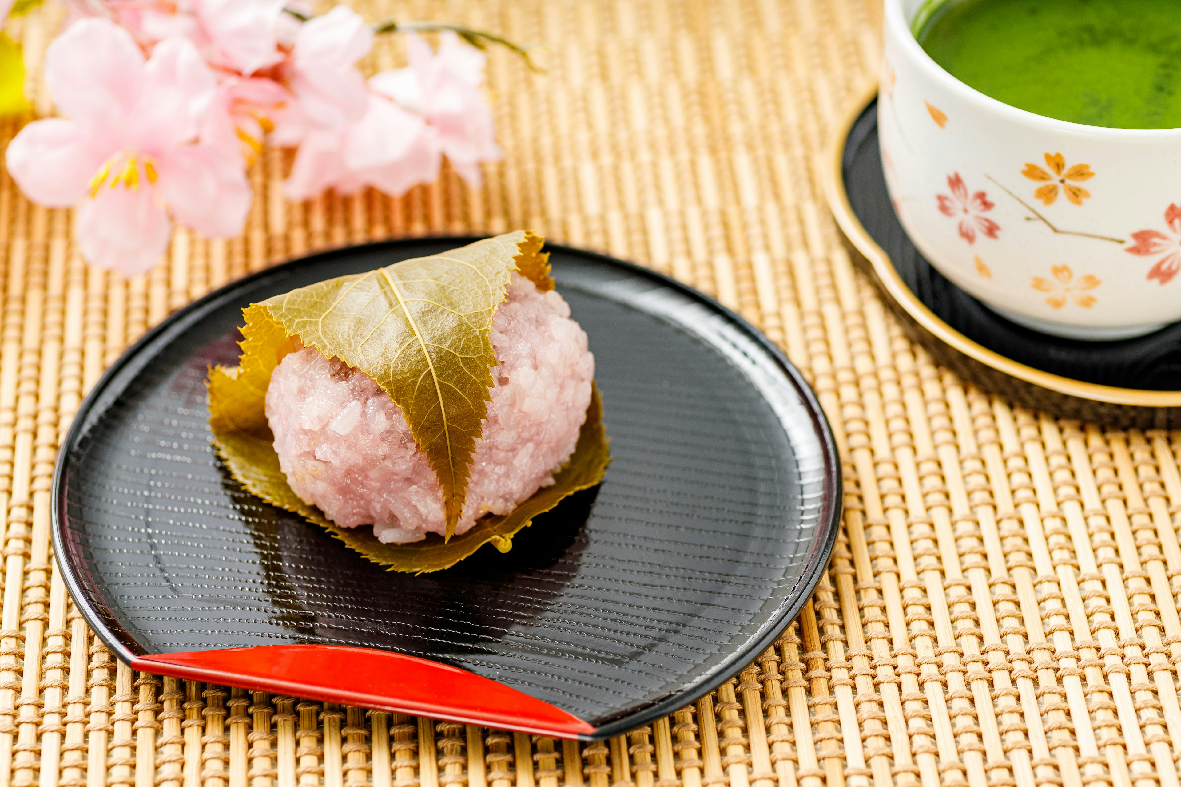 Hermosa presentación de sakura mochi junto a flores de cerezo y té verde