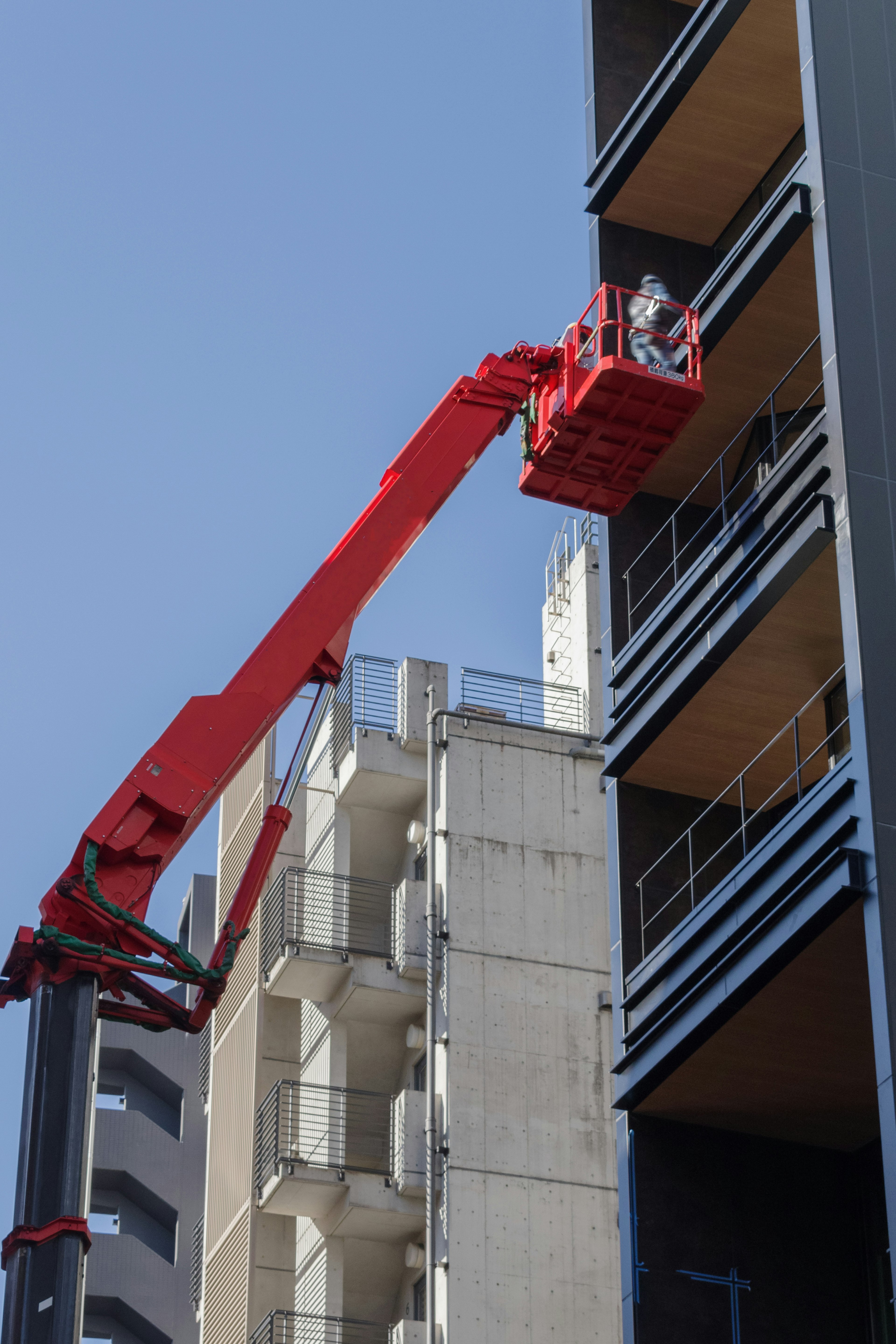 赤いクレーンが建物の外壁を作業する作業員を運ぶ