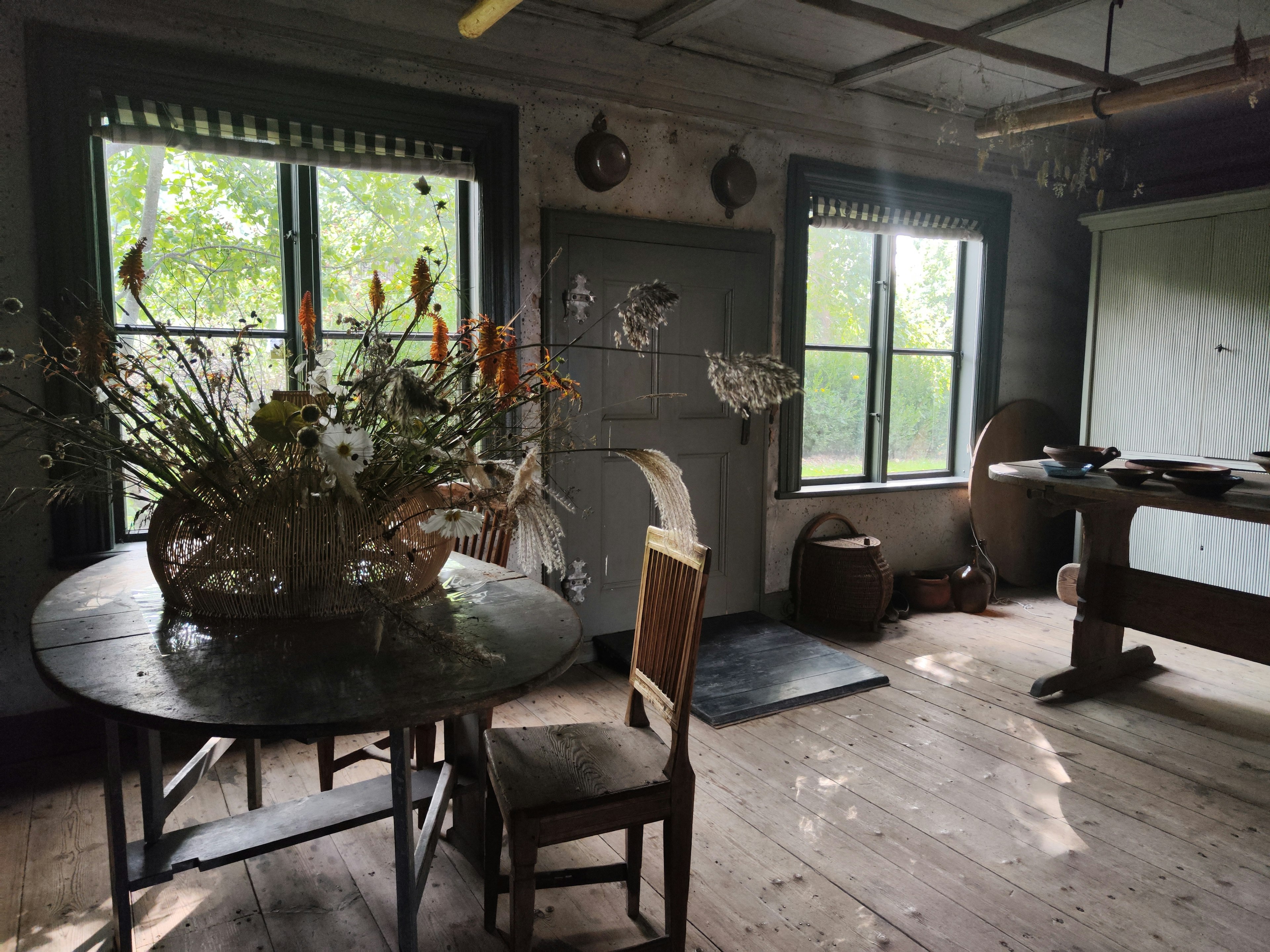 An old room with wooden table and chair natural light coming through the windows a vase of plants on the table